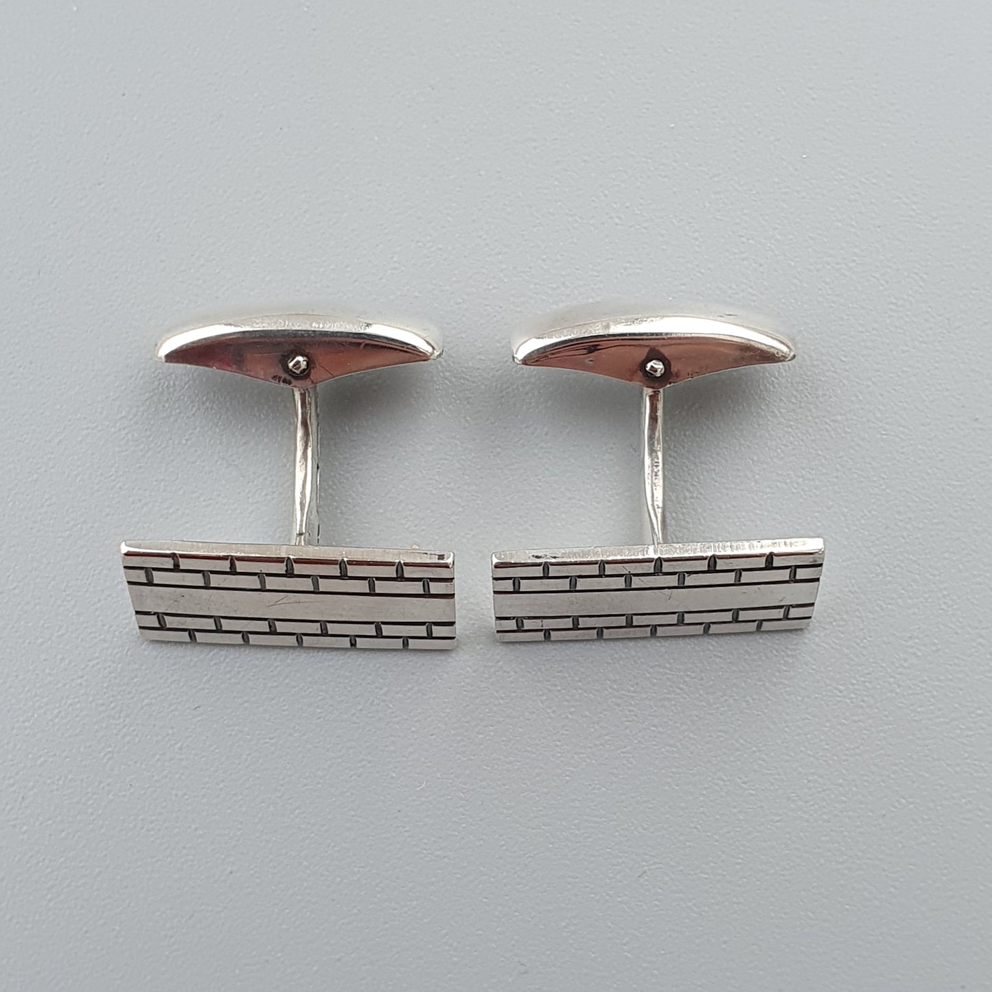 Pair of silver cufflinks with a brick pattern design.