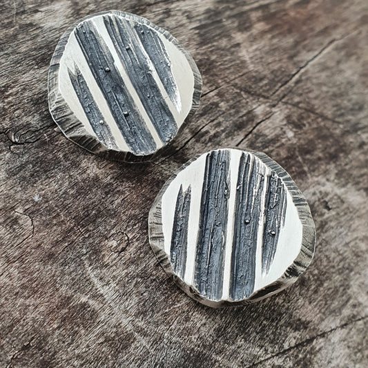 Pair of circular earrings or pendants with striped black and white patterns.