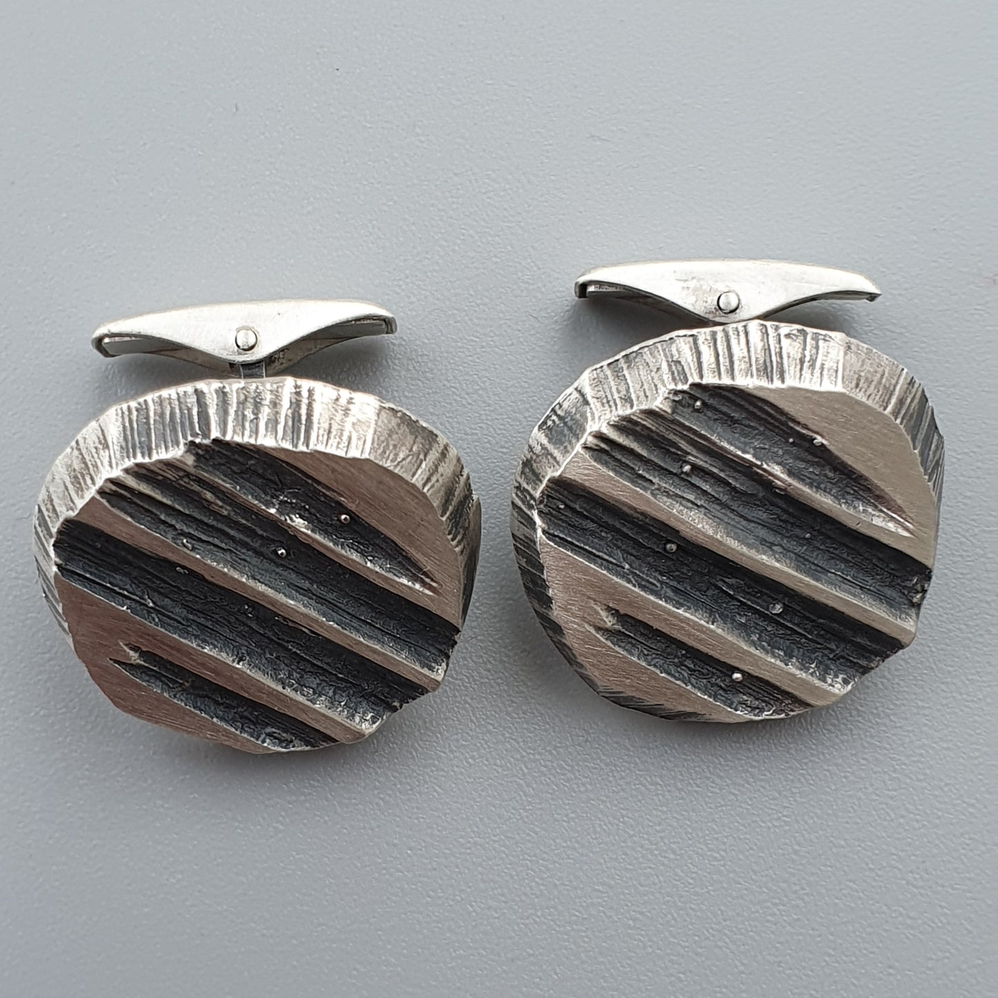 Pair of circular silver cufflinks with textured, striped designs.