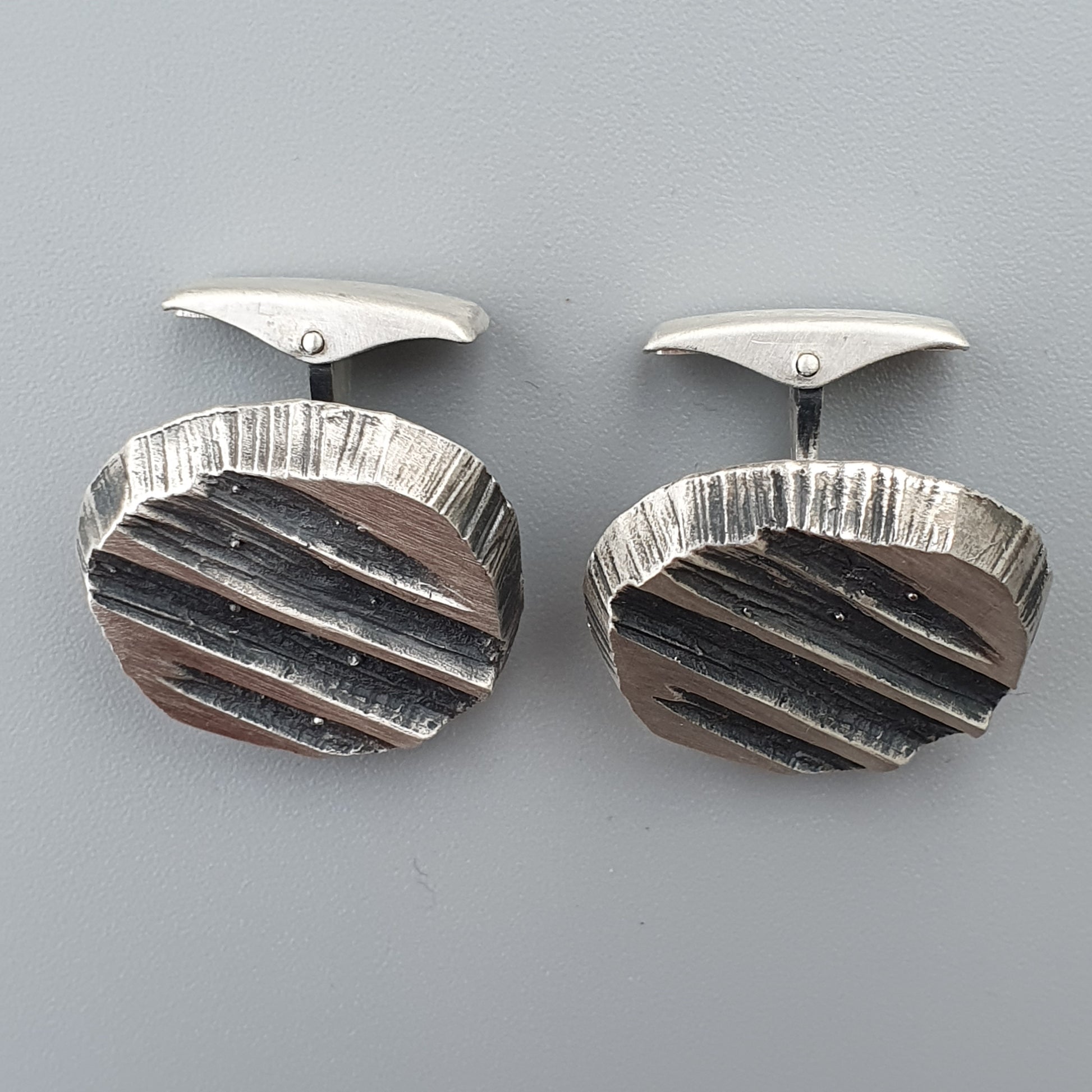 Pair of oval silver cufflinks with textured, striped designs.