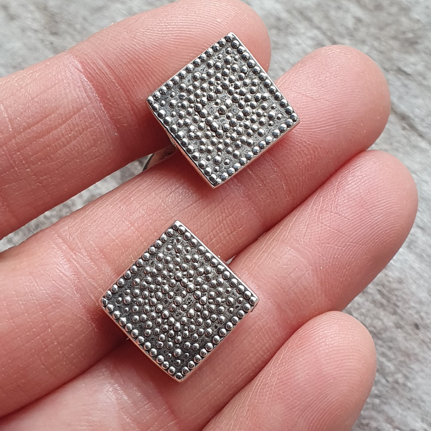 Square metal studs with a textured surface of tiny raised dots.