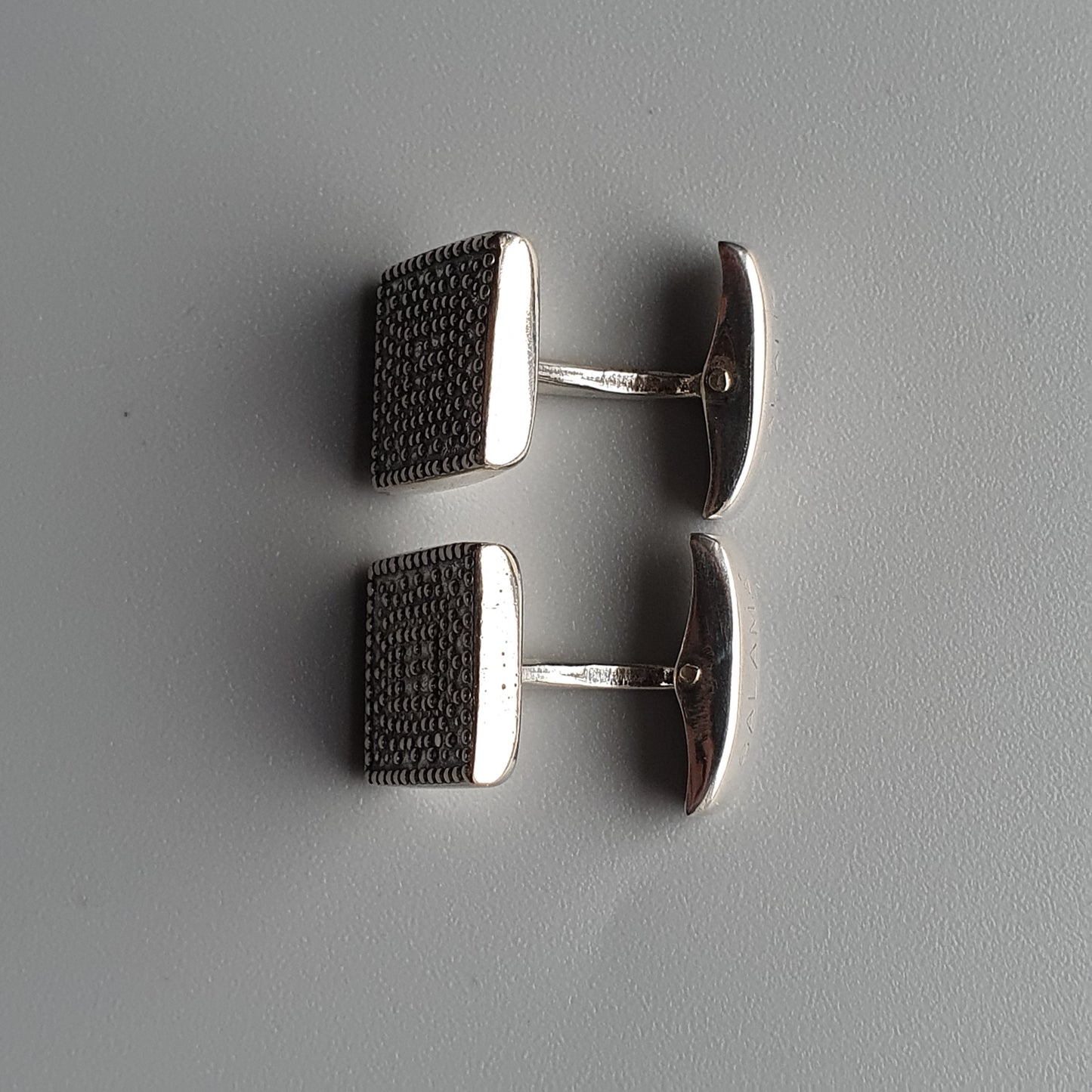 Pair of square silver cufflinks with textured dark surfaces.