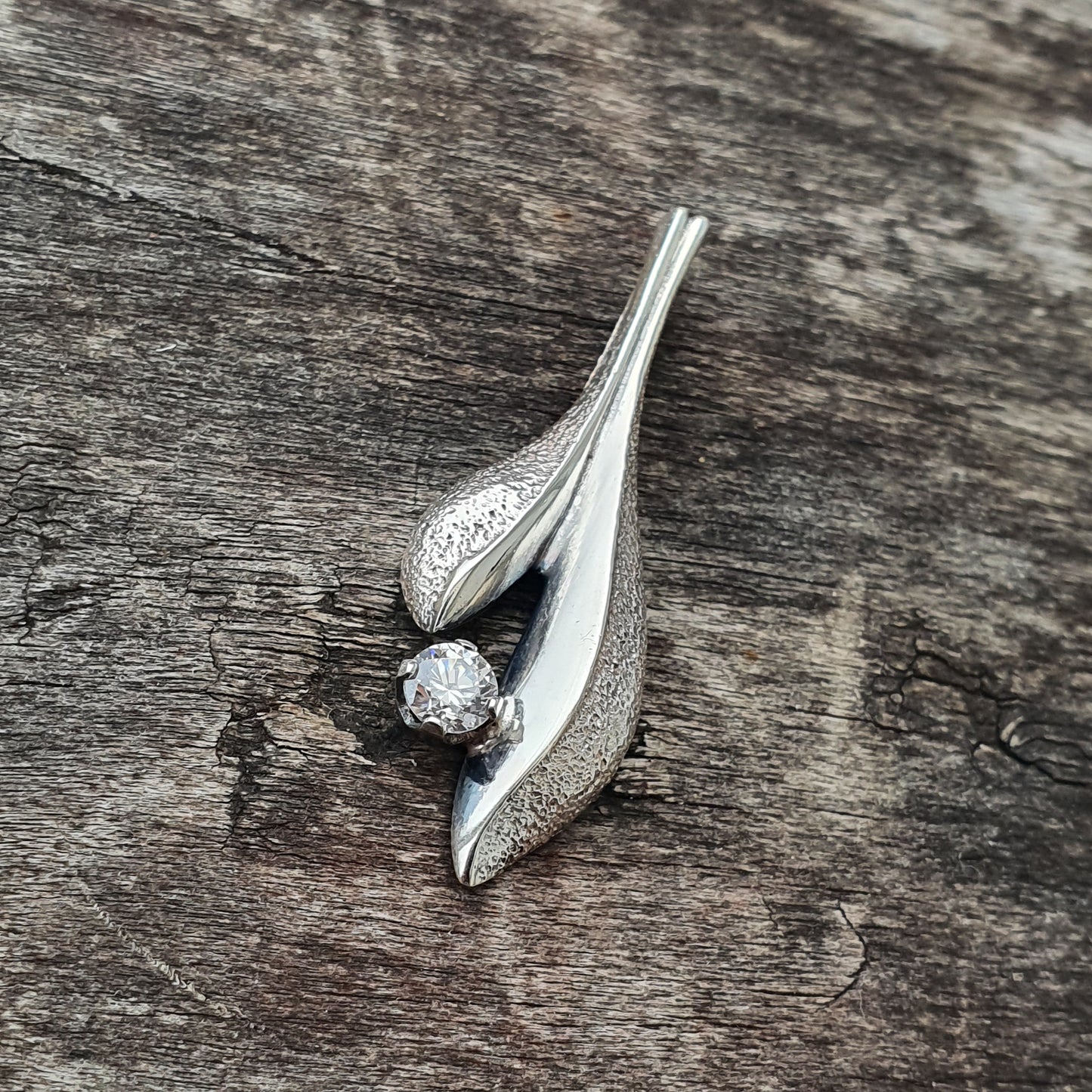 Silver brooch or pin shaped like stylized leaves or petals with a small gemstone.