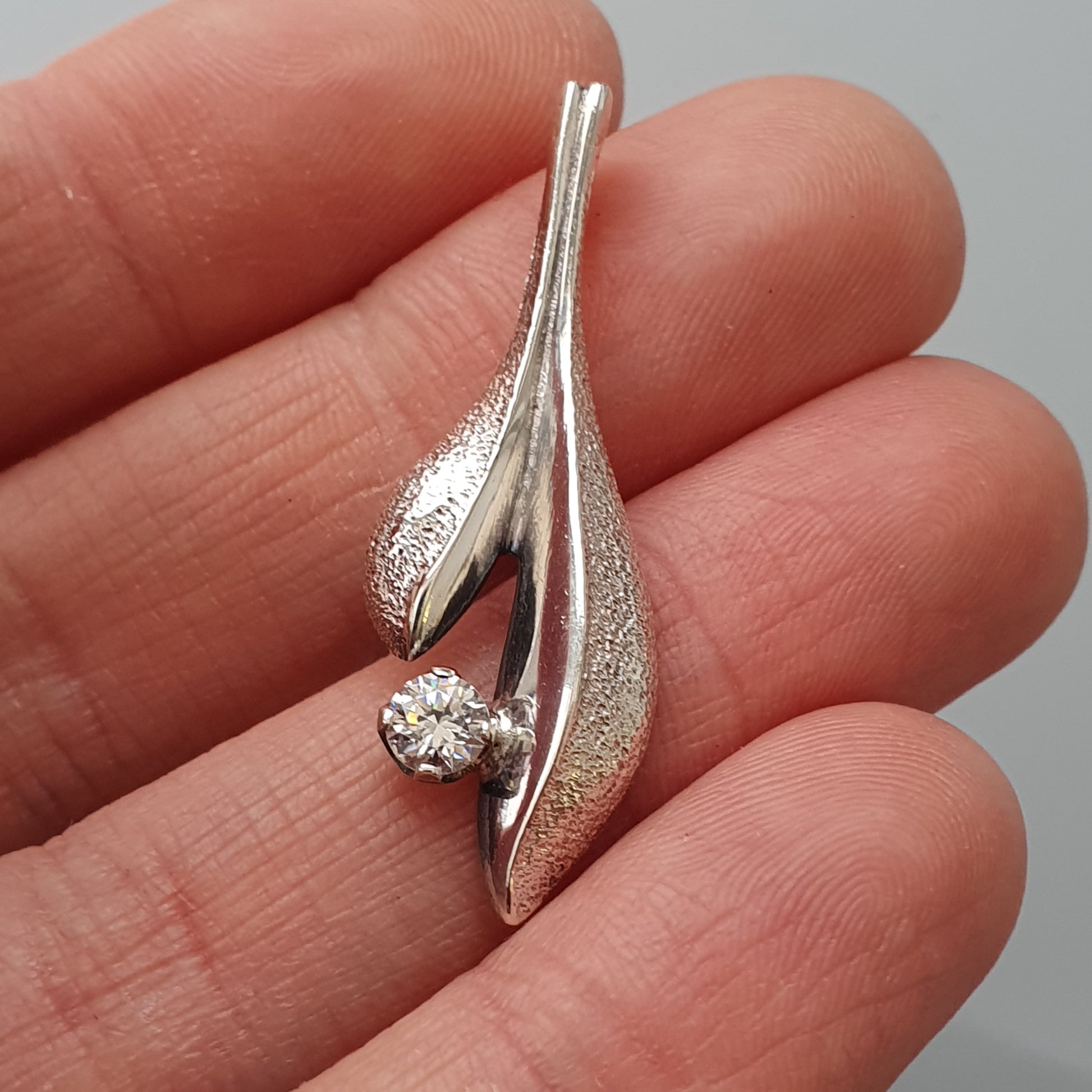 Silver pendant with a curved, leaf-like design featuring a single diamond.