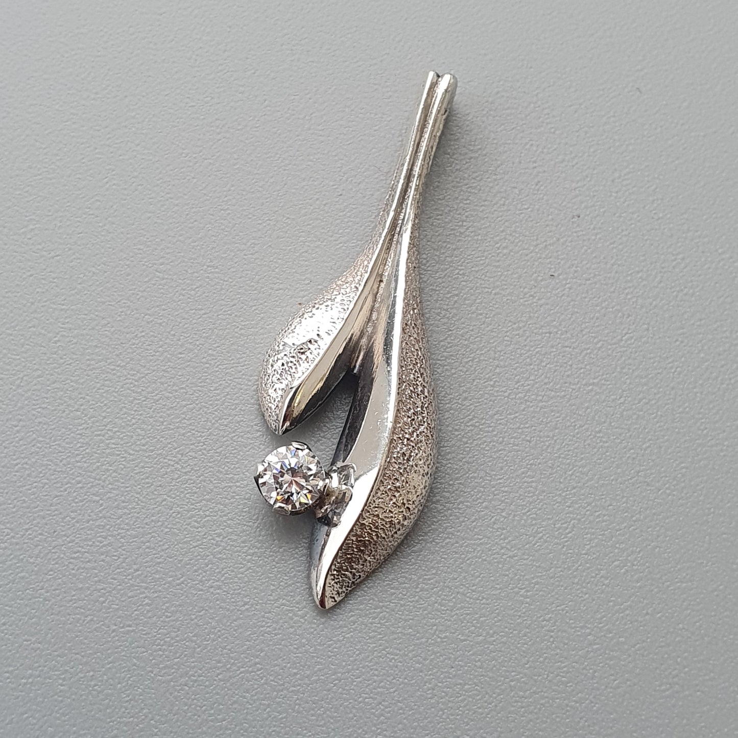 Silver pendant with a teardrop-shaped design featuring a small diamond.