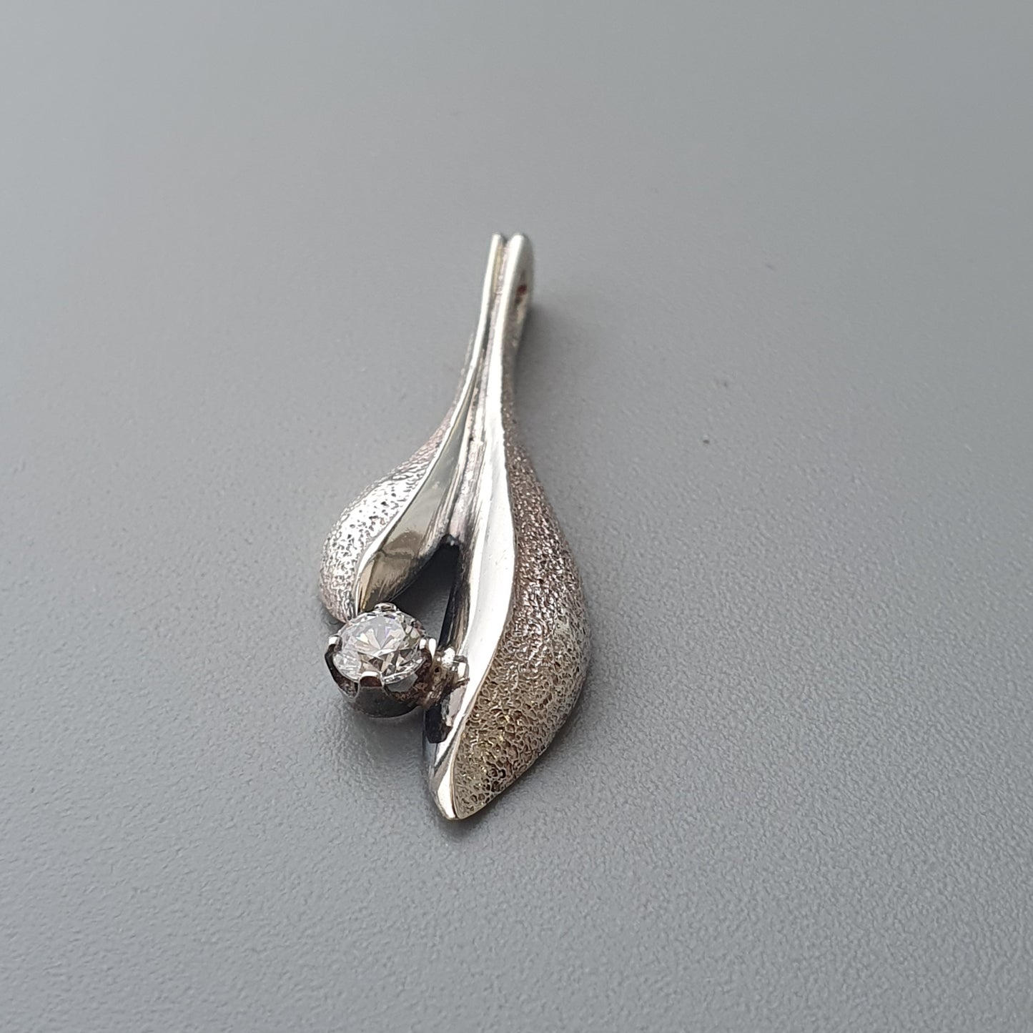 Silver pendant with a curved leaf-like design and a small gemstone.