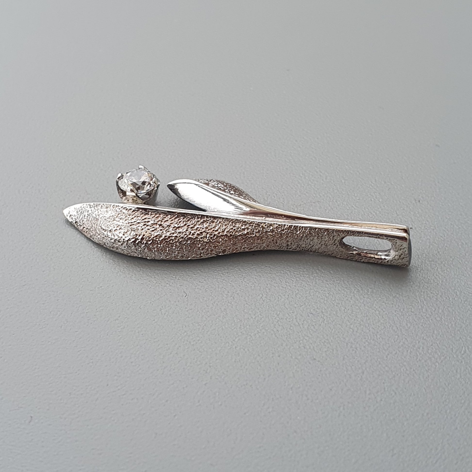 Silver brooch shaped like a leaf or feather with a small gemstone accent.