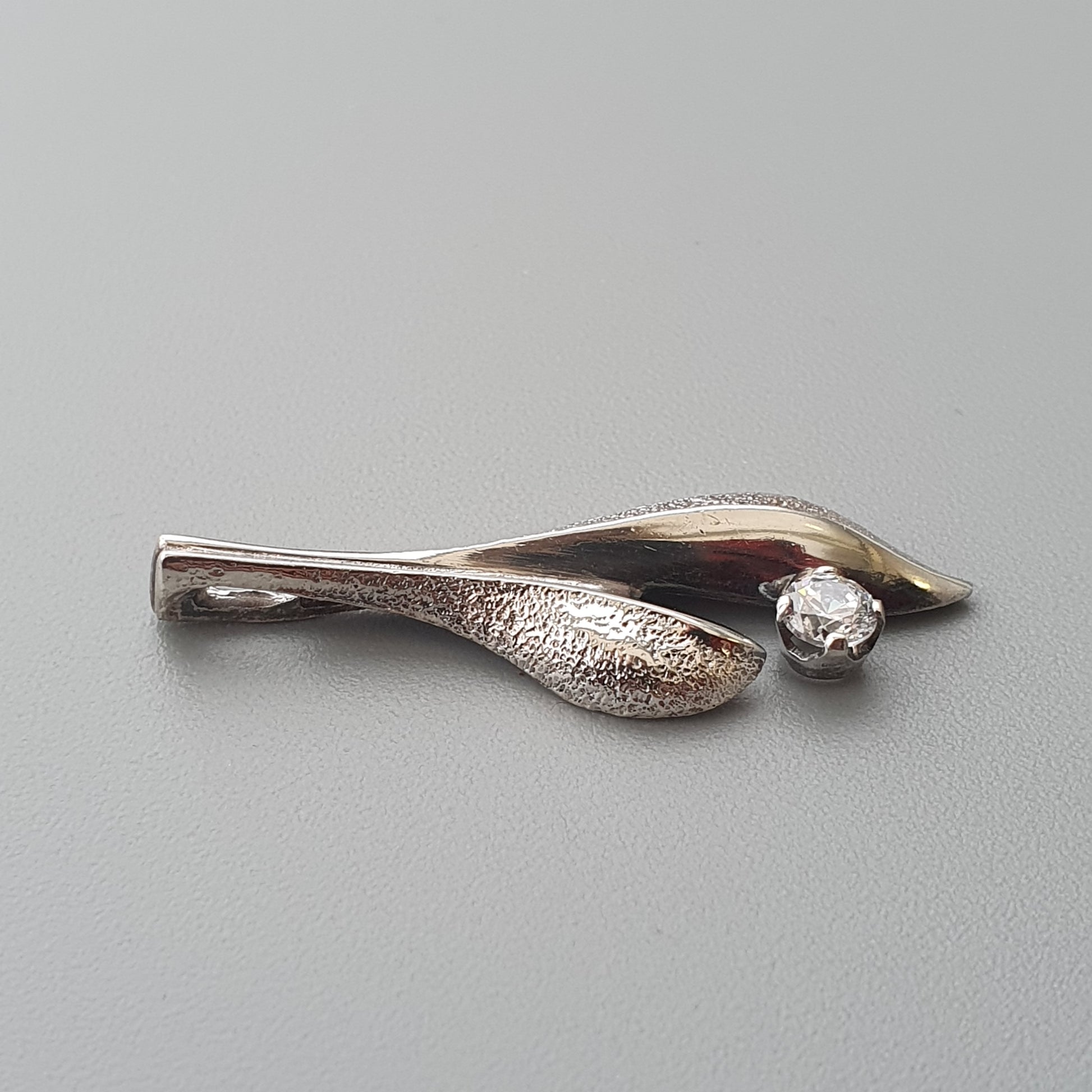 Silver brooch shaped like a stylized leaf or petal with a small gemstone accent.