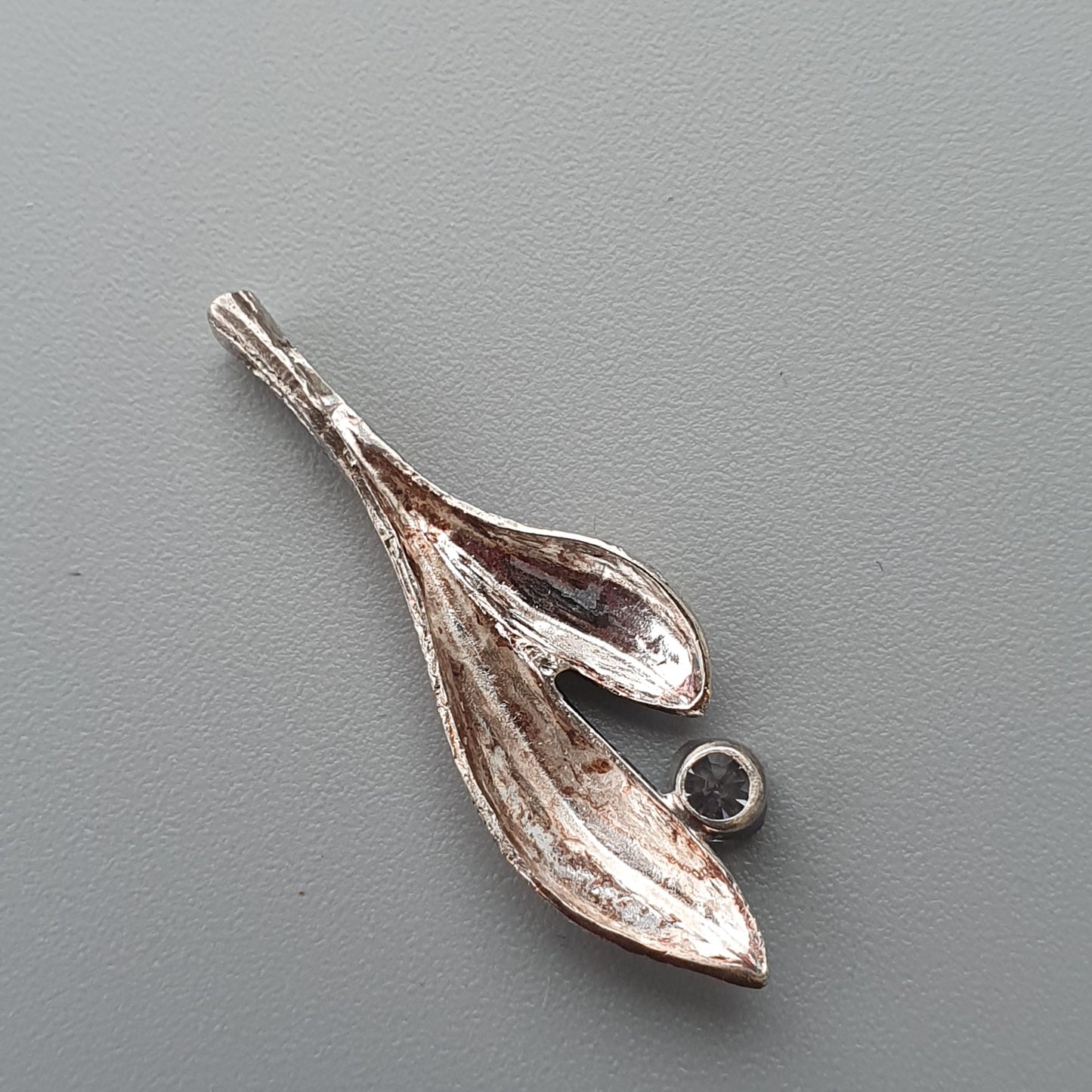 Silver-toned pendant shaped like stylized leaves or petals with a small dark gemstone.