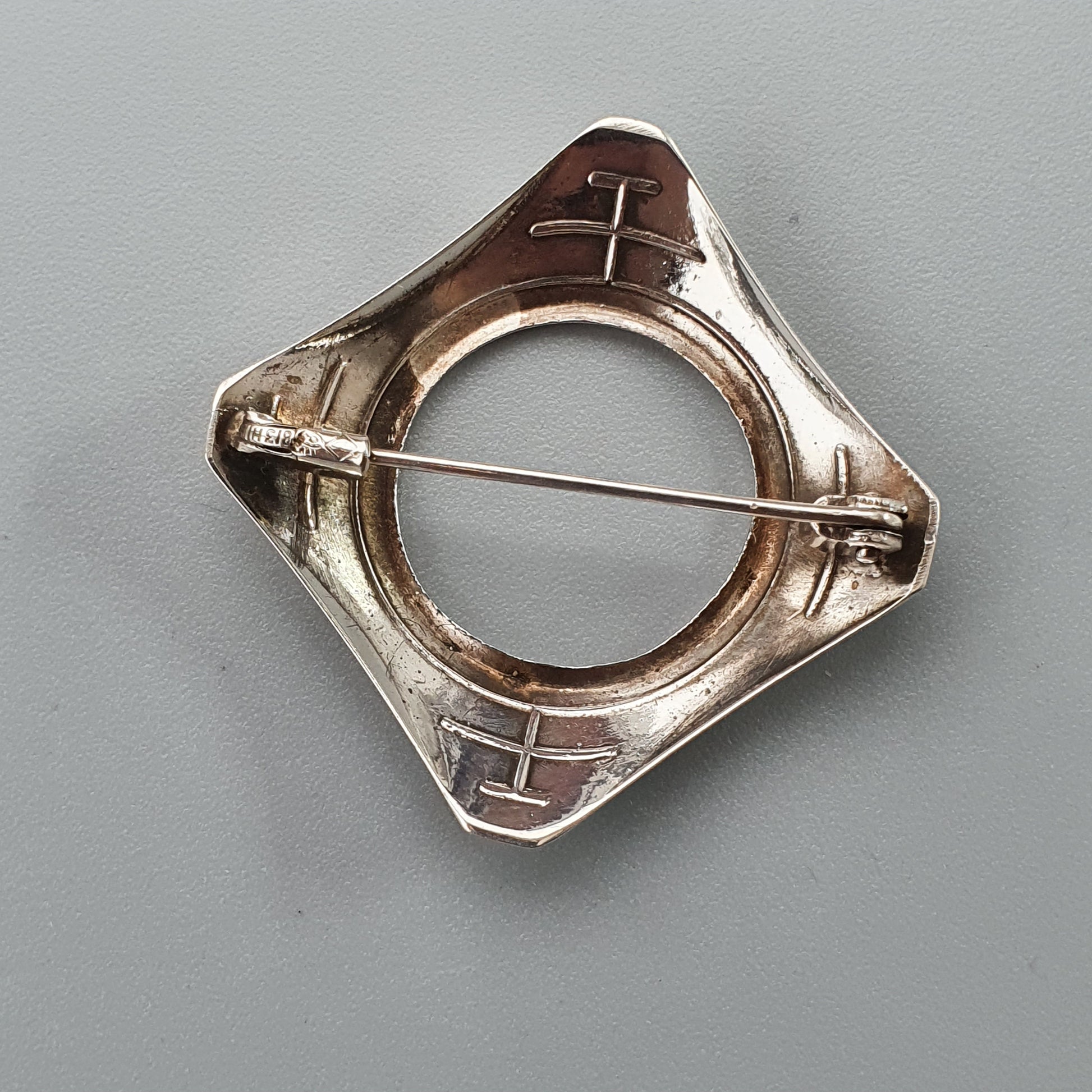 Silver brooch or pin with a square-shaped frame and a central bar crossing through it.