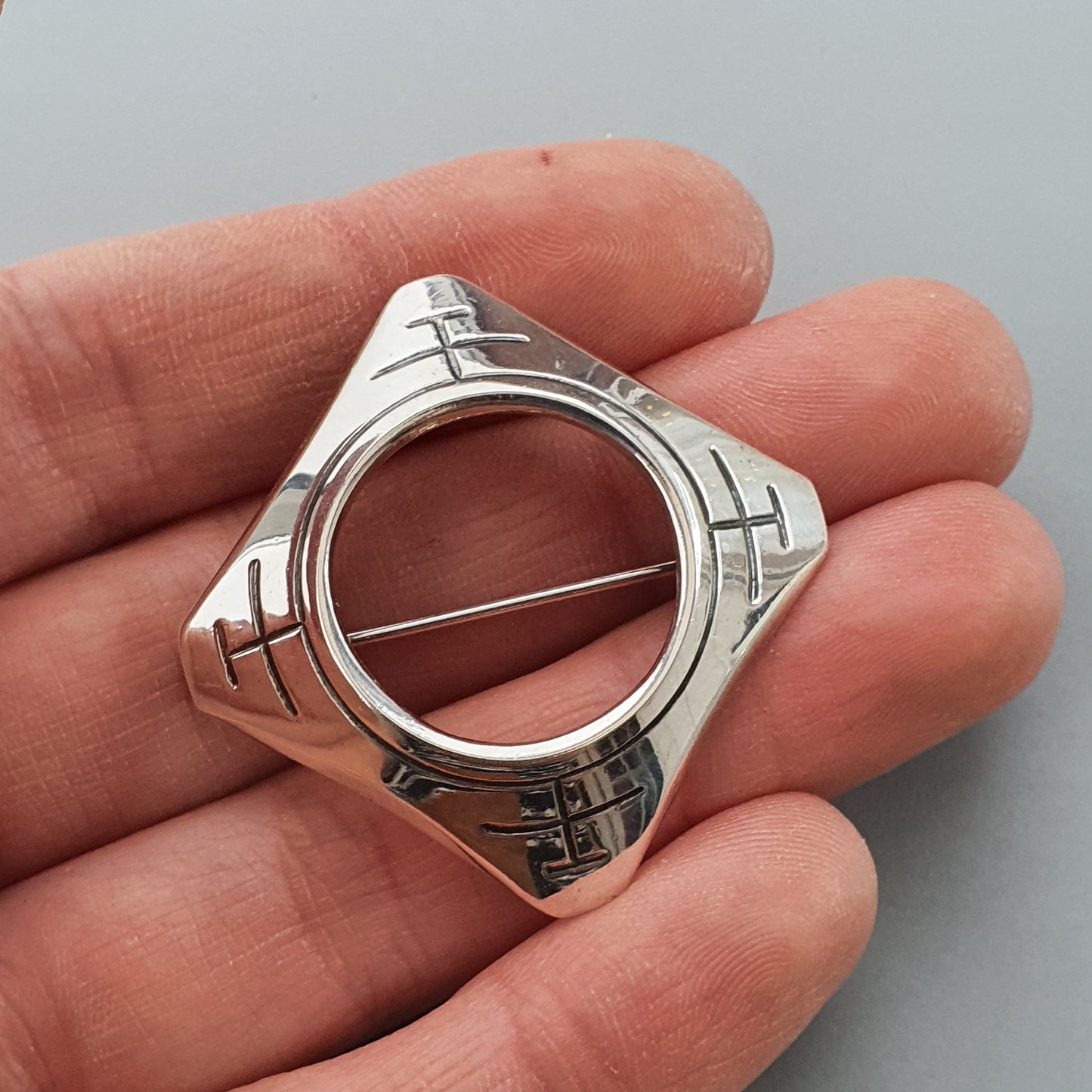 Silver geometric brooch or pin with a circular opening in the center.