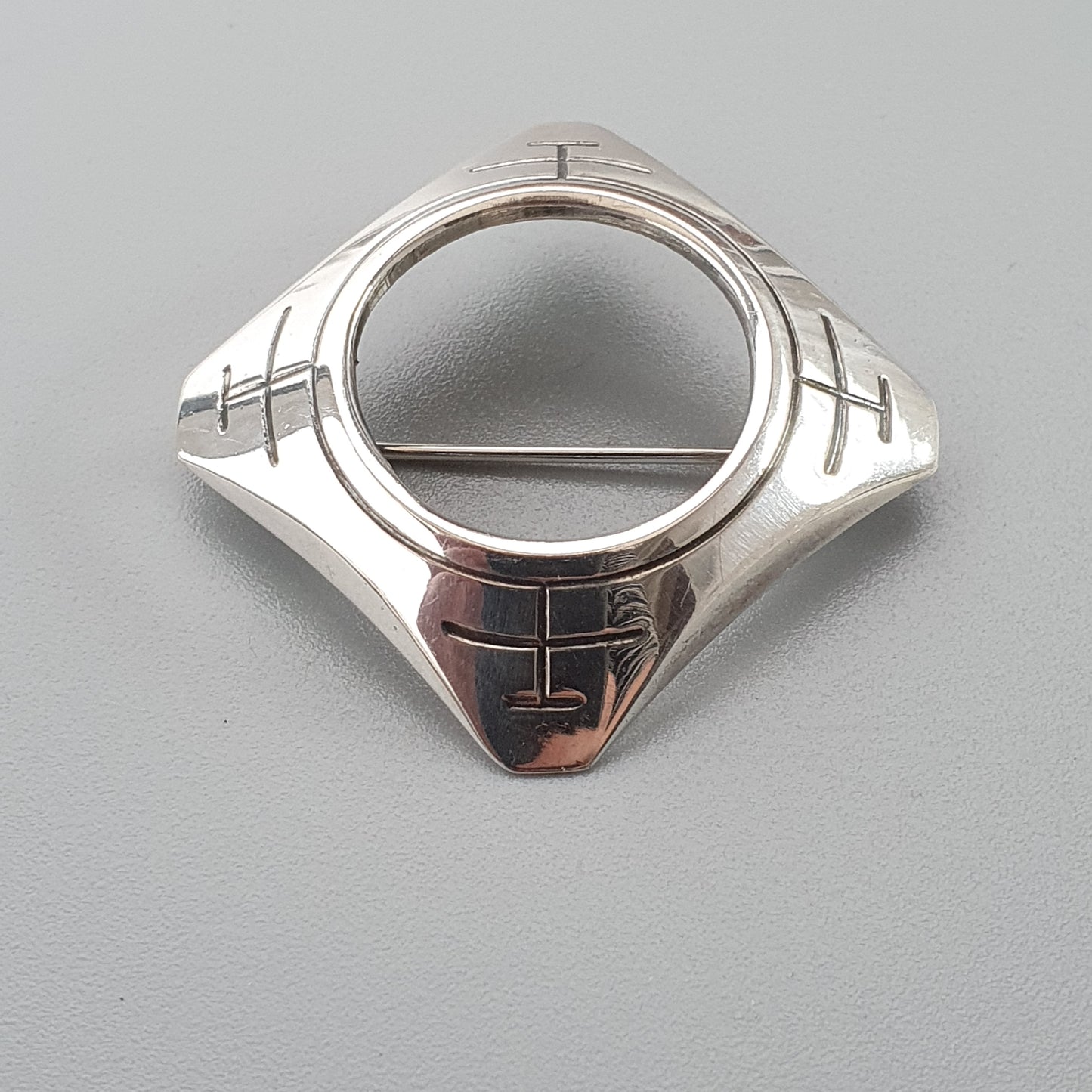 Silver ring with a circular center and geometric designs on the sides.