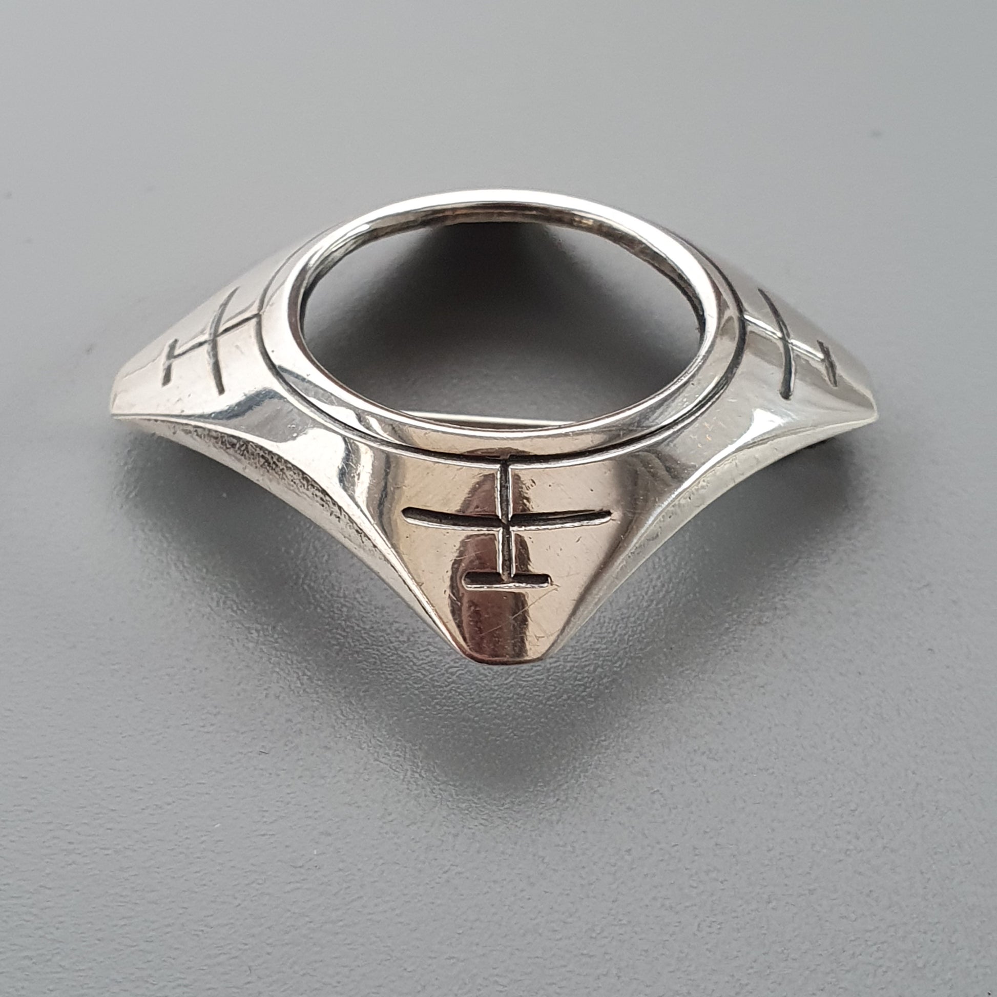 Silver ring with a dark circular center and geometric designs on the band.