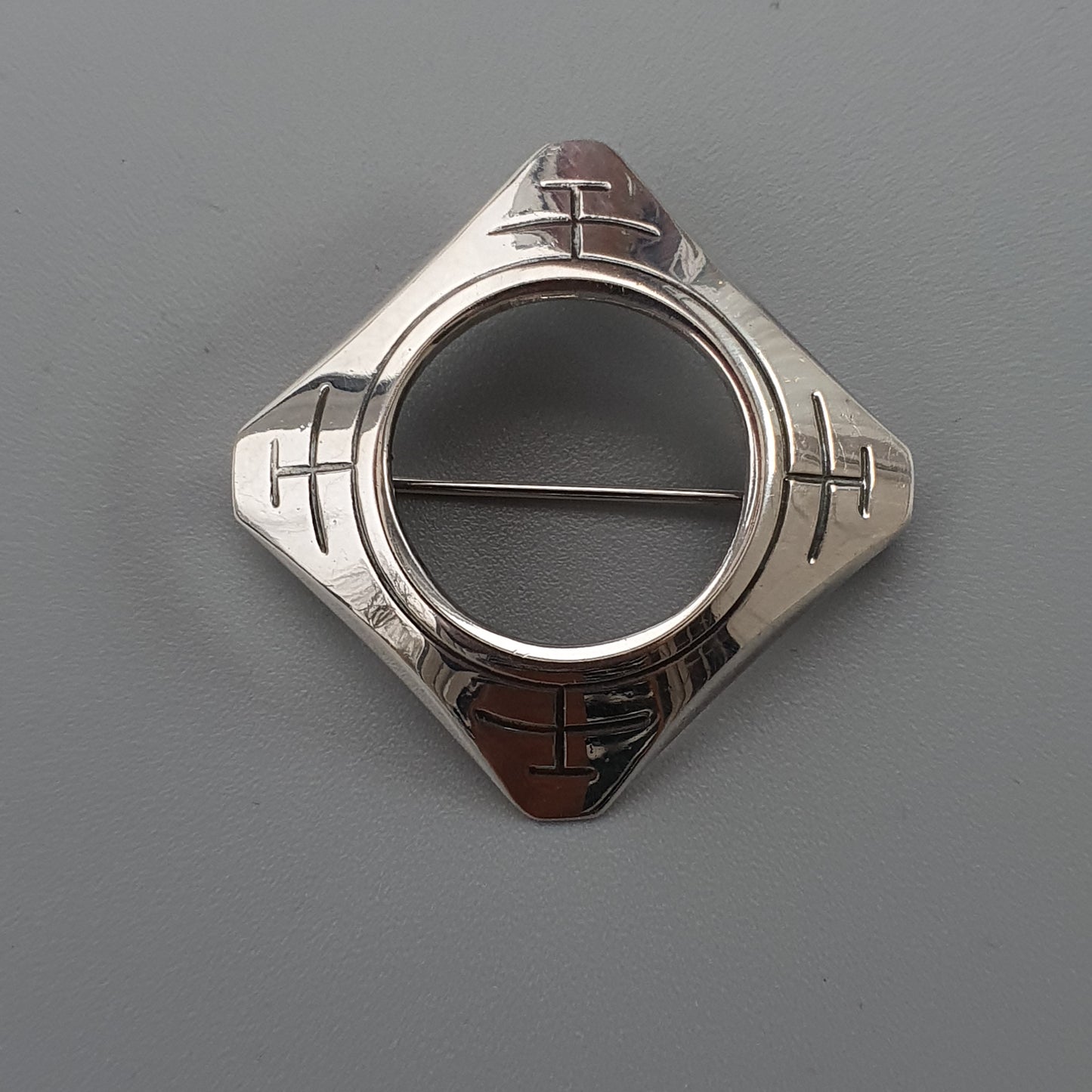 Silver brooch or pin with a circular center and geometric design.