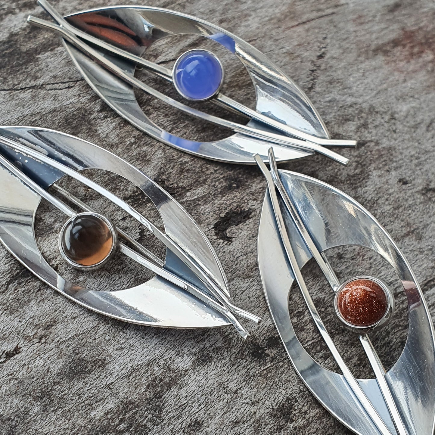 Eye-shaped silver brooches with colorful gemstones in the center.