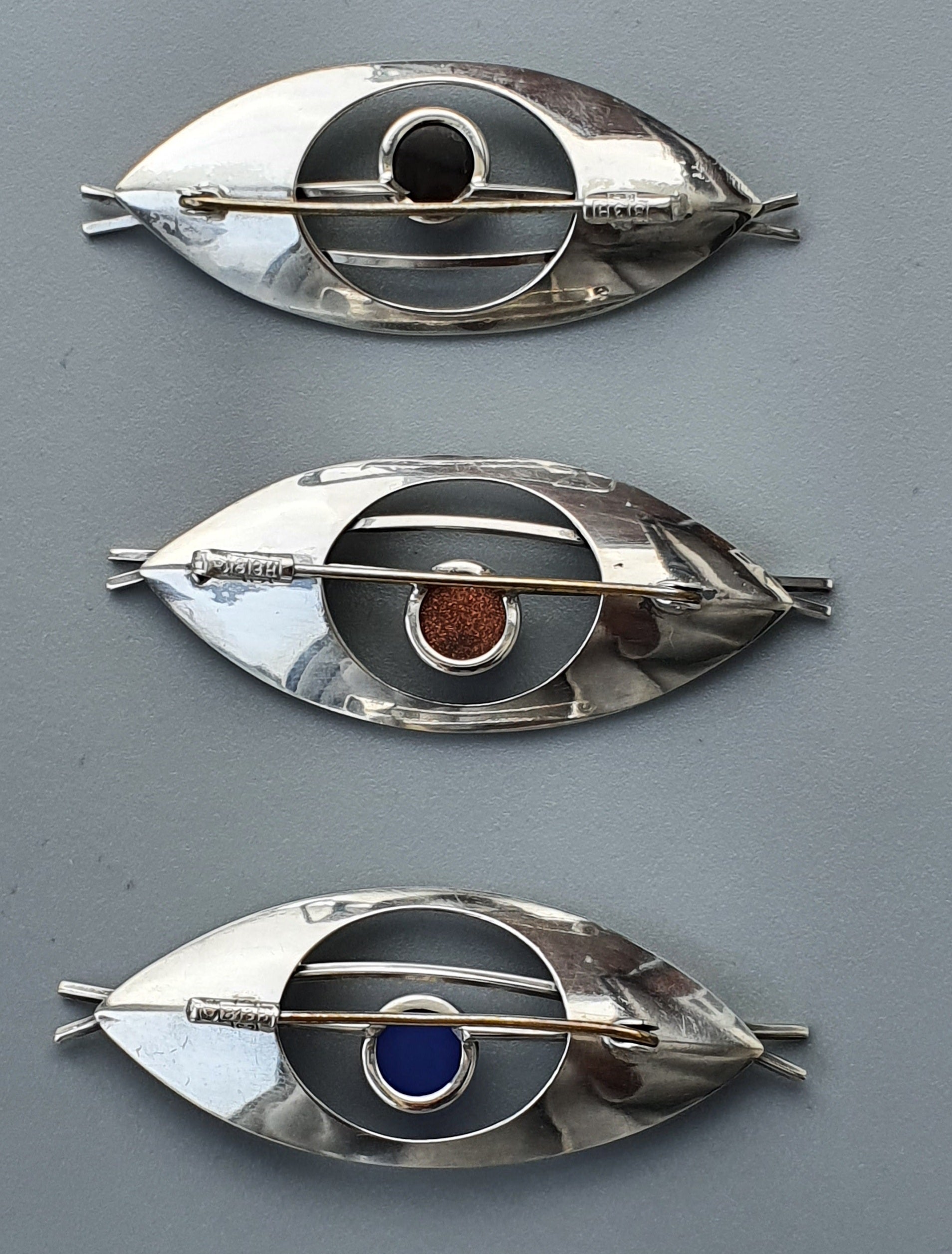 Eye-shaped metallic brooches or pins with colored inlays.