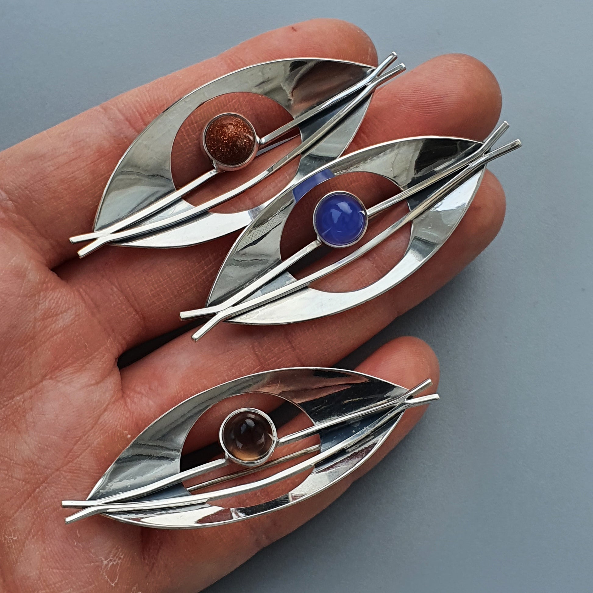 Eye-shaped silver brooches with colorful gemstones in the center.