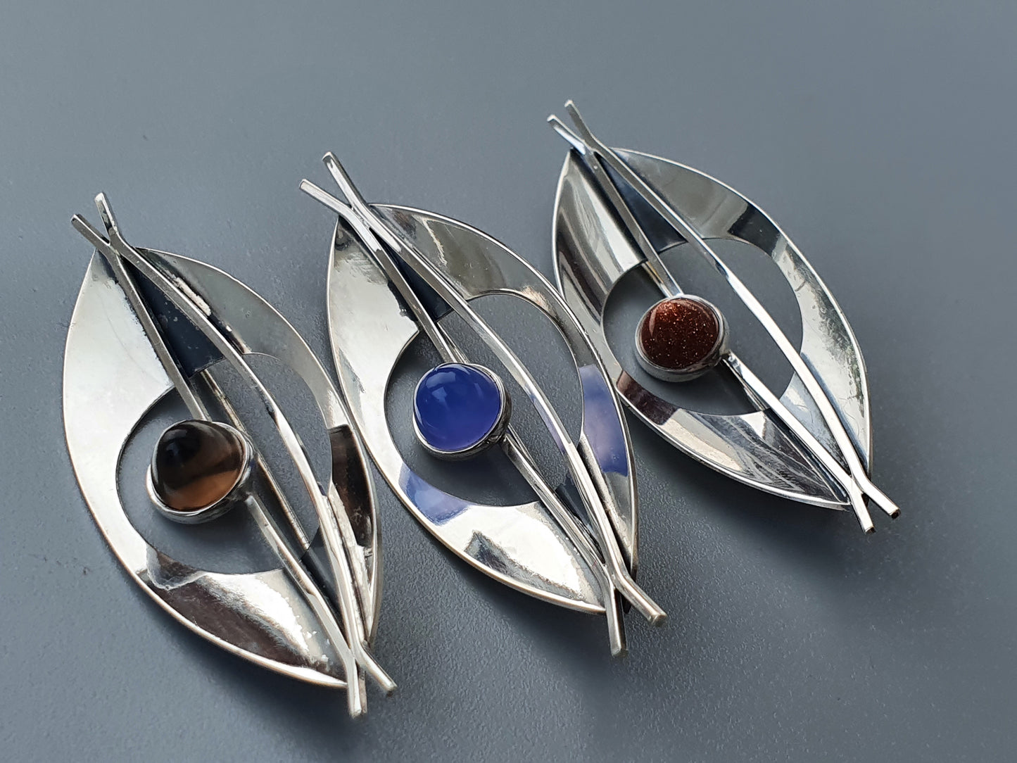 Set of three modernist silver brooches with colored gemstone accents.