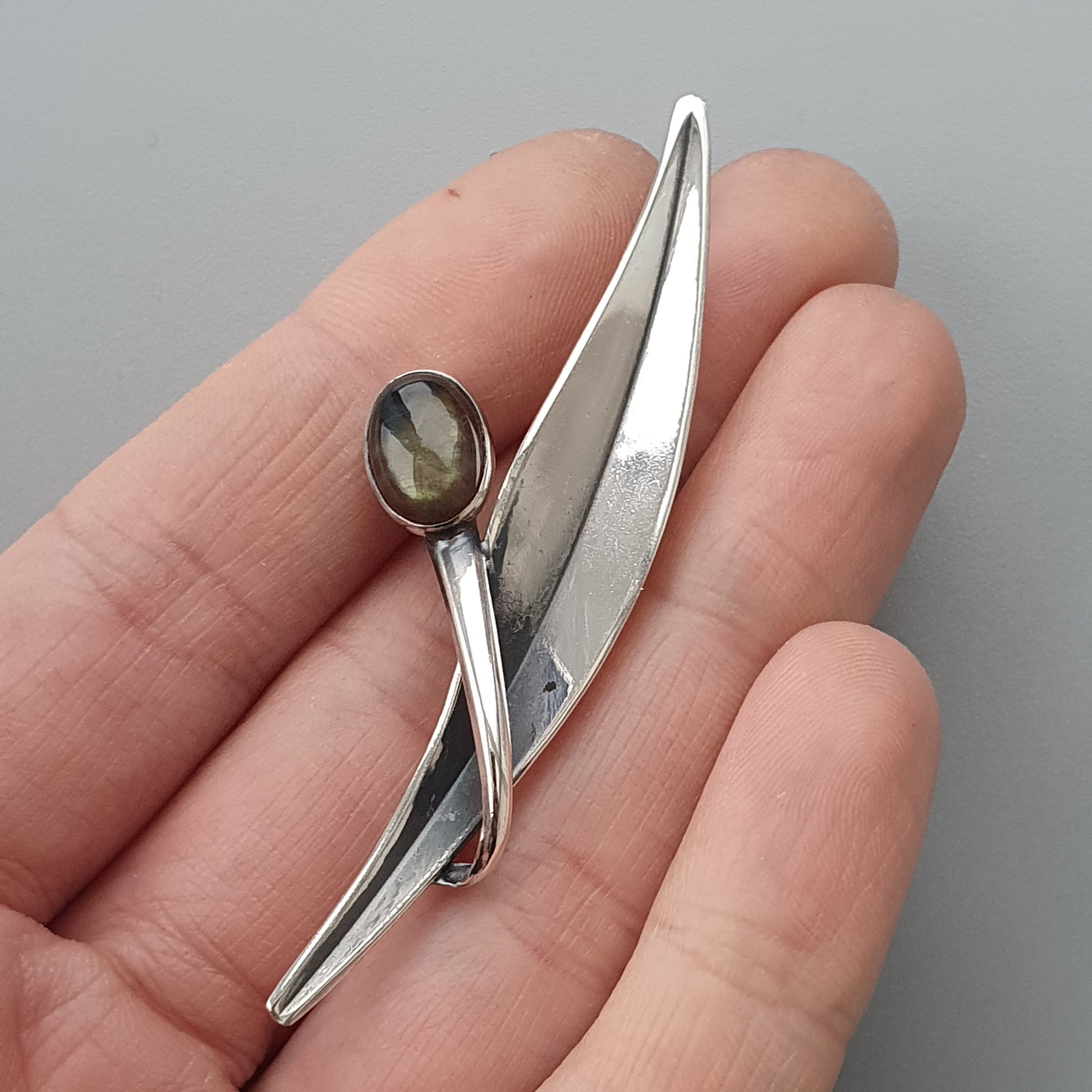 Silver brooch or pin shaped like an abstract figure with a gemstone accent.