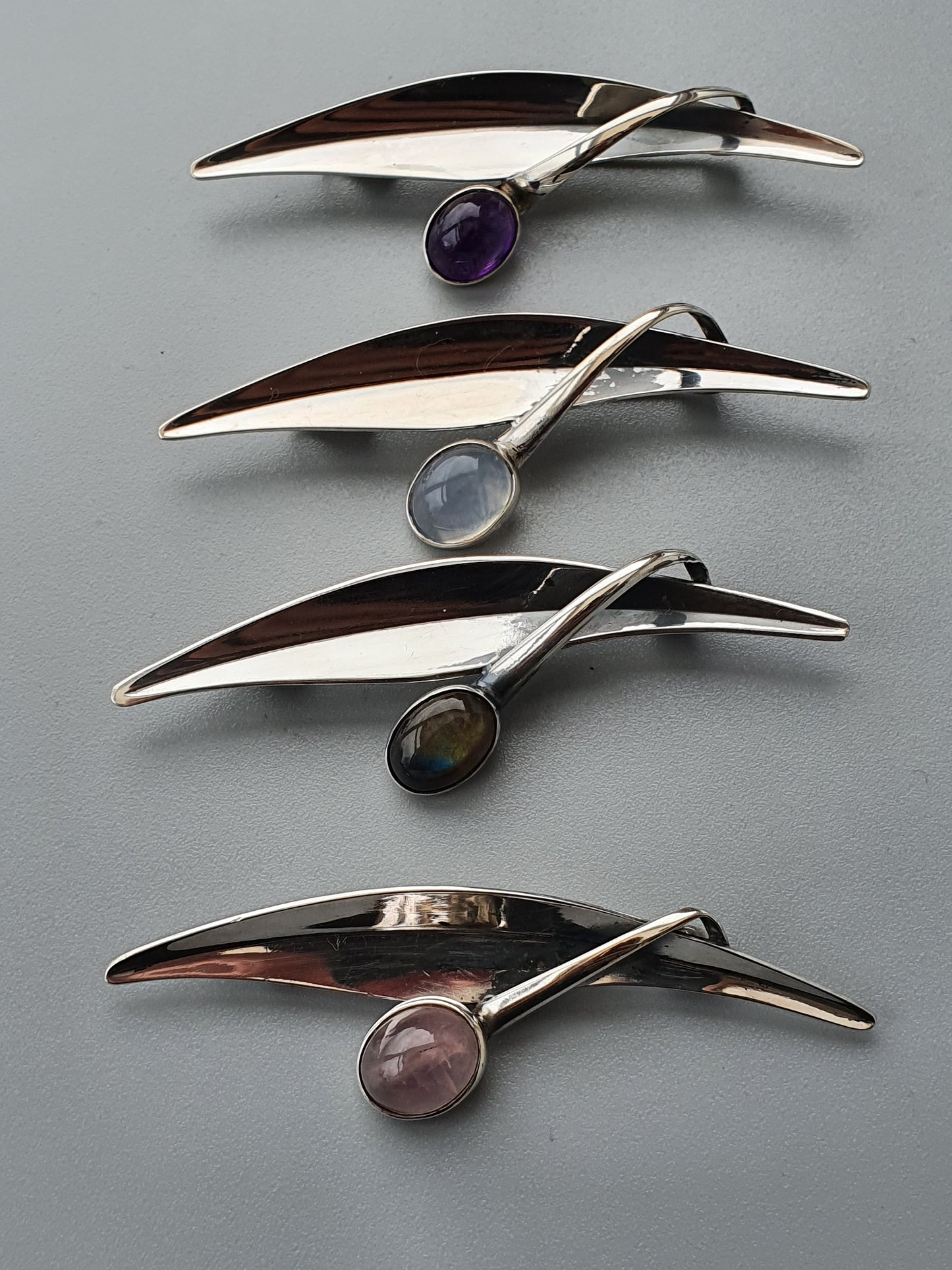 Set of four sleek, curved metal brooches or pins with gemstone accents.