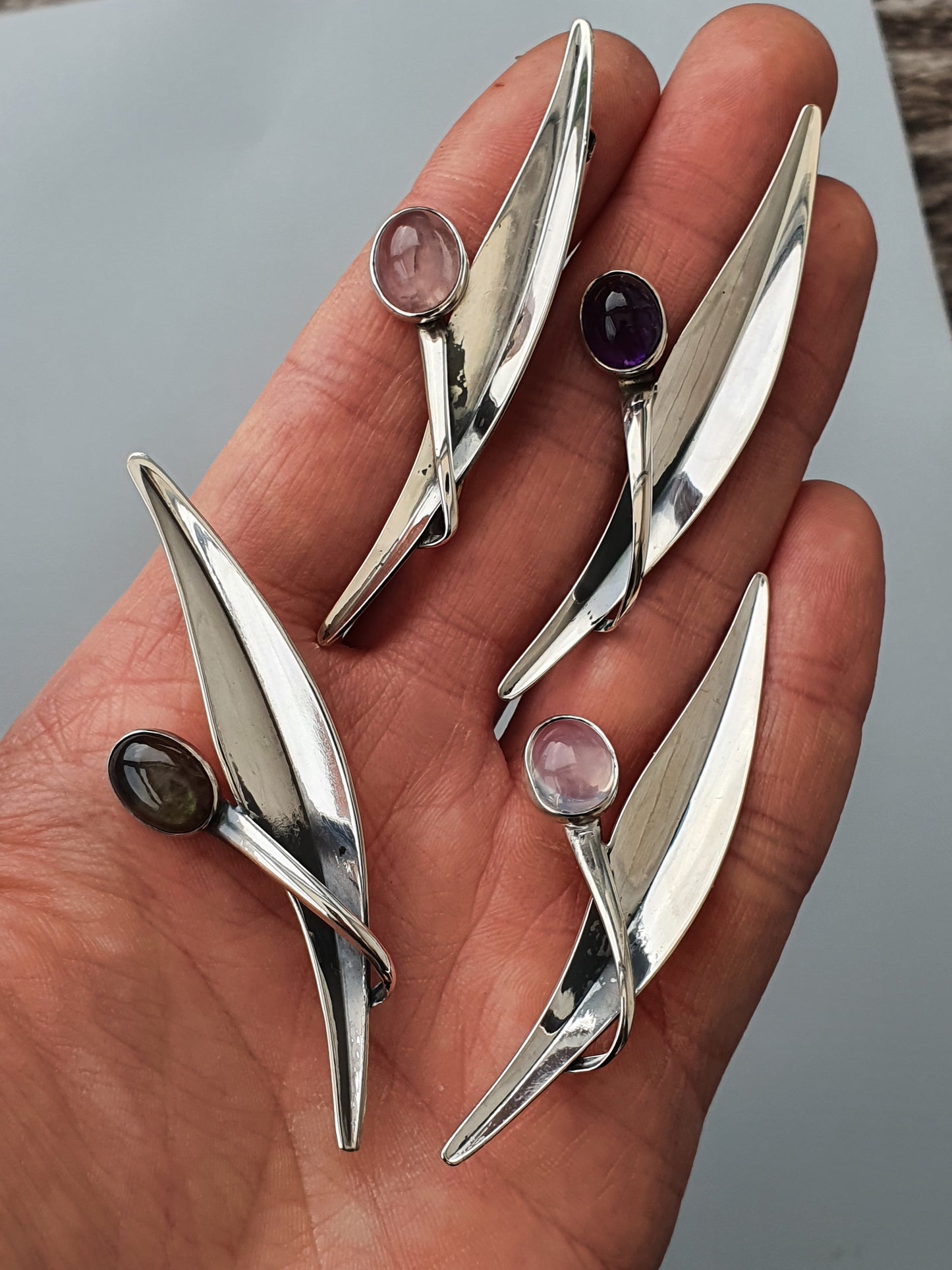 Silver jewelry pieces shaped like elongated leaves or abstract birds with gemstone accents.