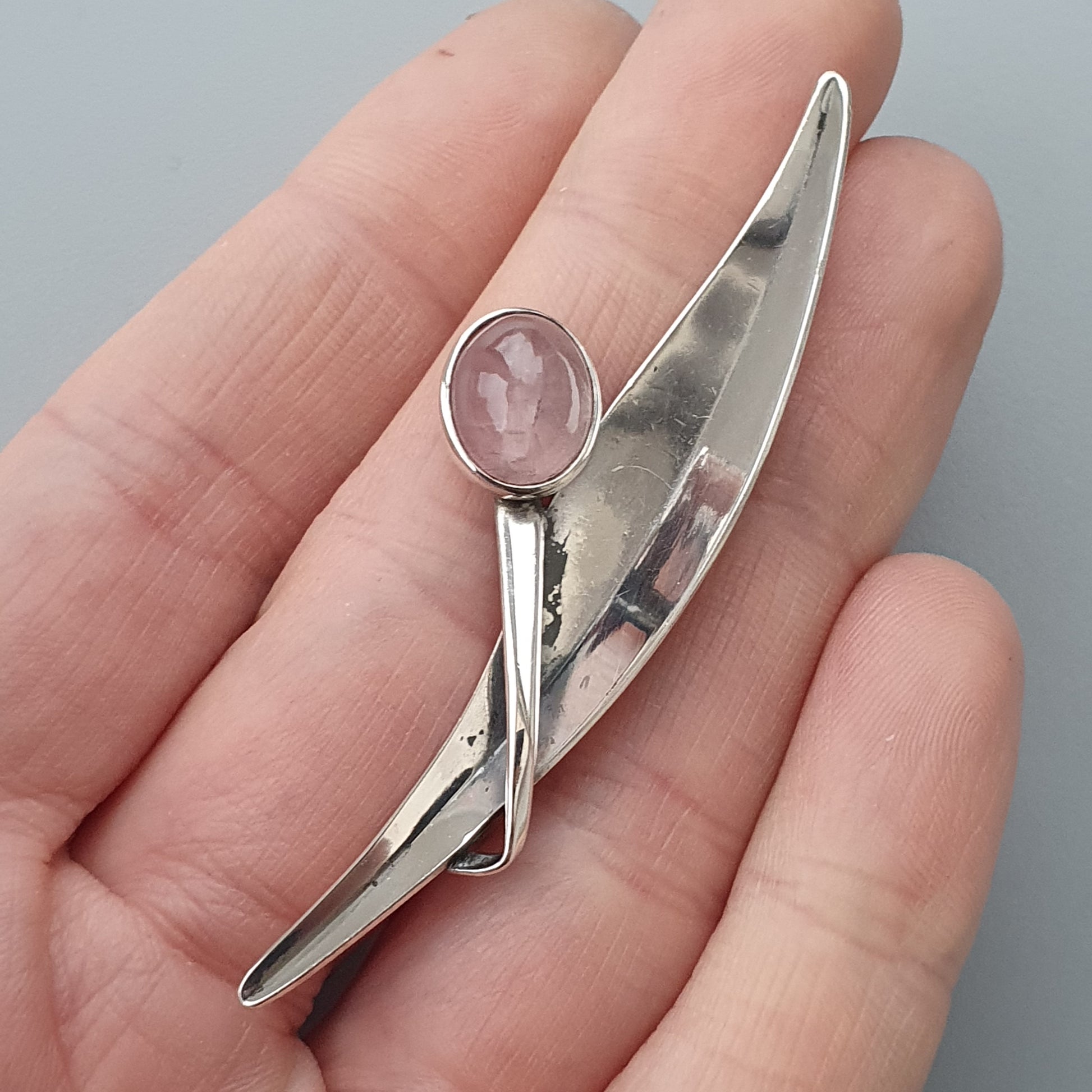 Silver brooch or pin with an abstract design and a pink gemstone.