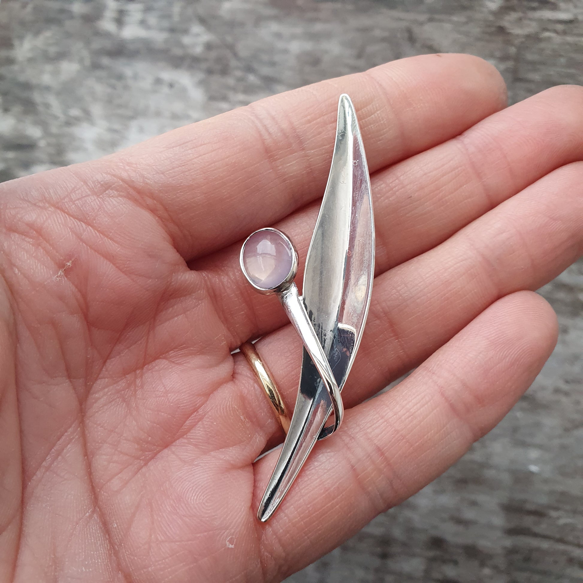 Silver brooch or pin with an elongated leaf shape and a small round gemstone.