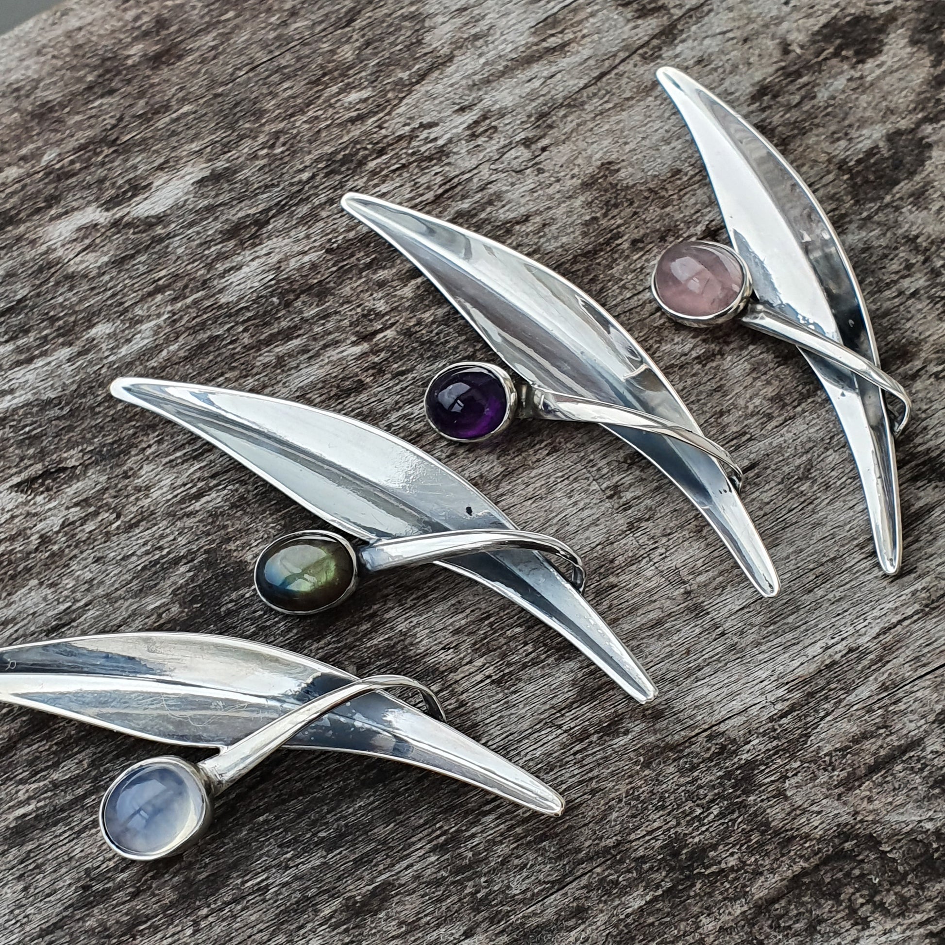 Sleek silver brooches shaped like elongated leaves, each adorned with a colorful gemstone.