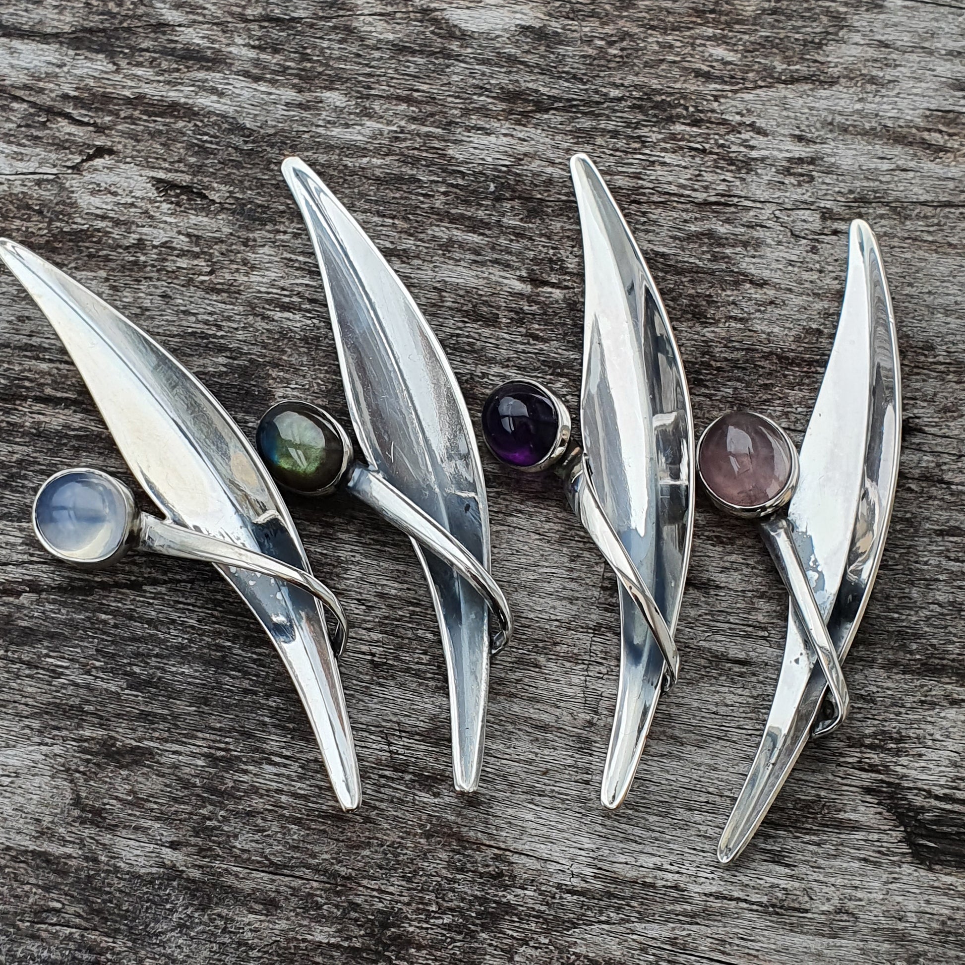 Silver leaf-shaped brooches or pendants with colorful gemstones.