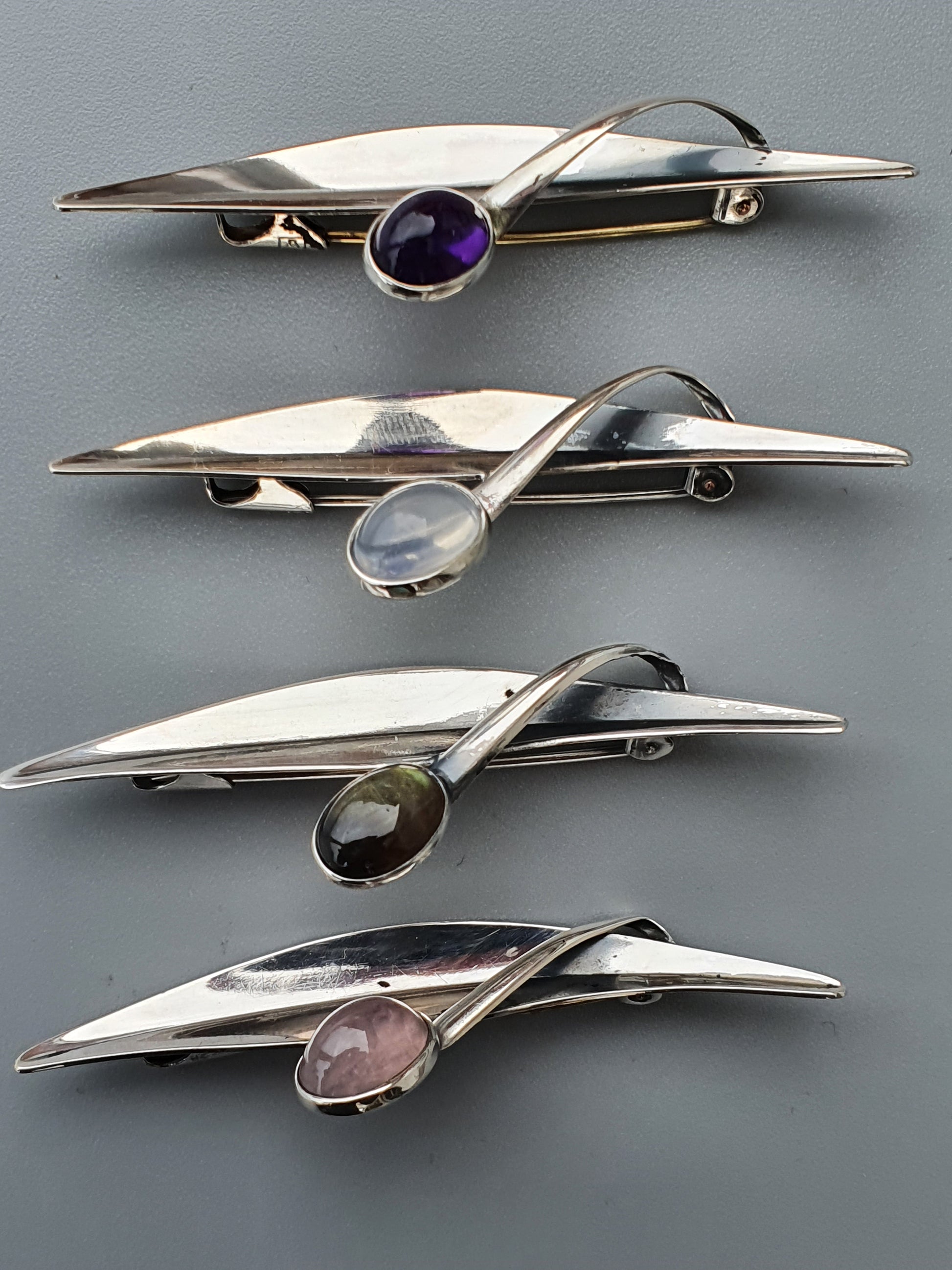 Sleek, futuristic brooches or pins featuring elongated metallic shapes with inset gemstones.