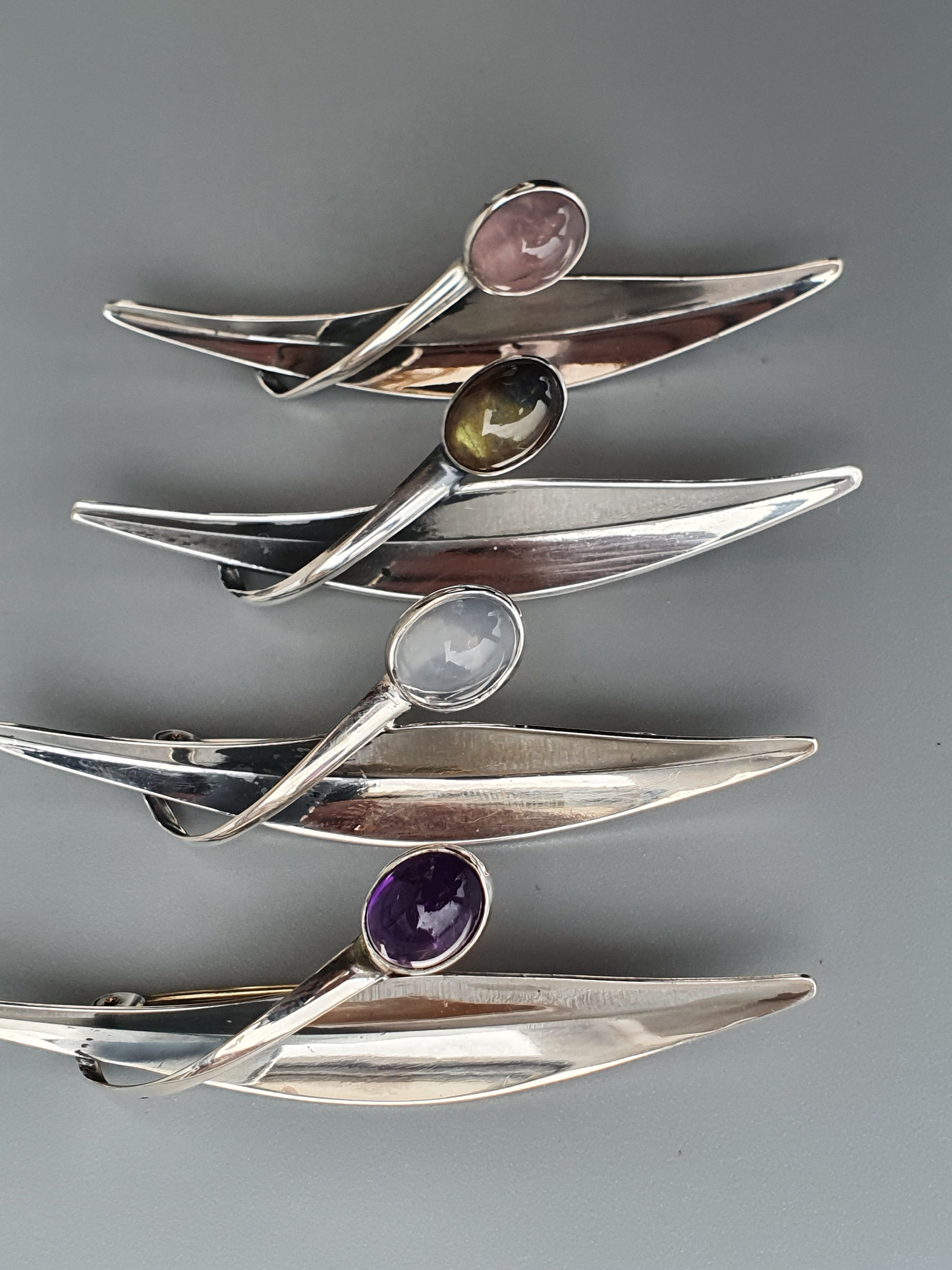 Set of four sleek, modernist silver brooches with colorful gemstones.