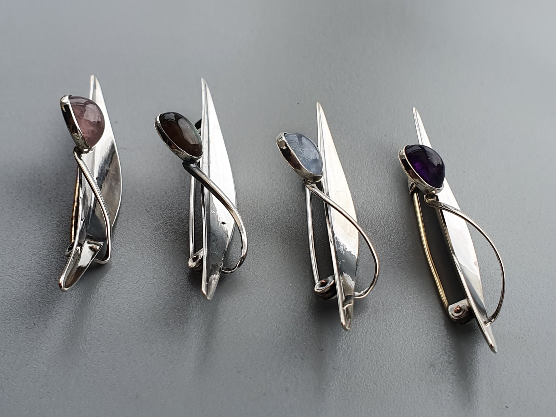 Four silver brooches or pins with geometric designs and gemstones.