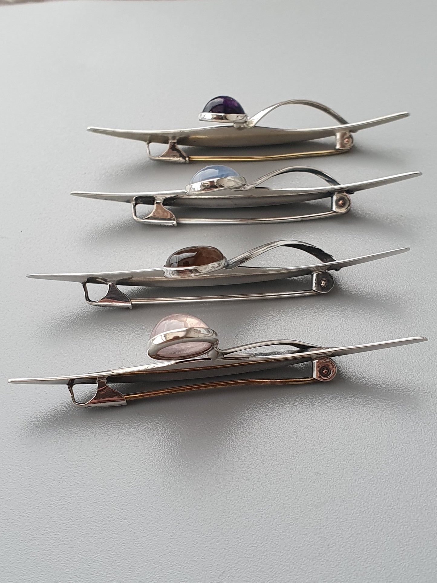 Sleek, modernist silver brooches with smooth stones or gems set into curved metal designs.