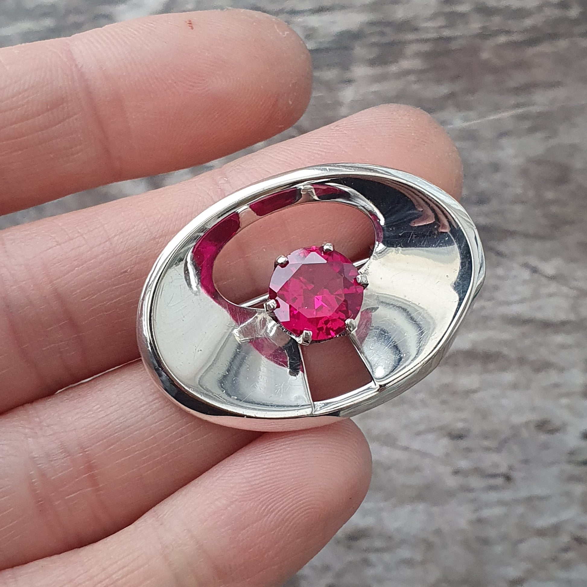 Silver oval brooch or pendant featuring a central pink gemstone.