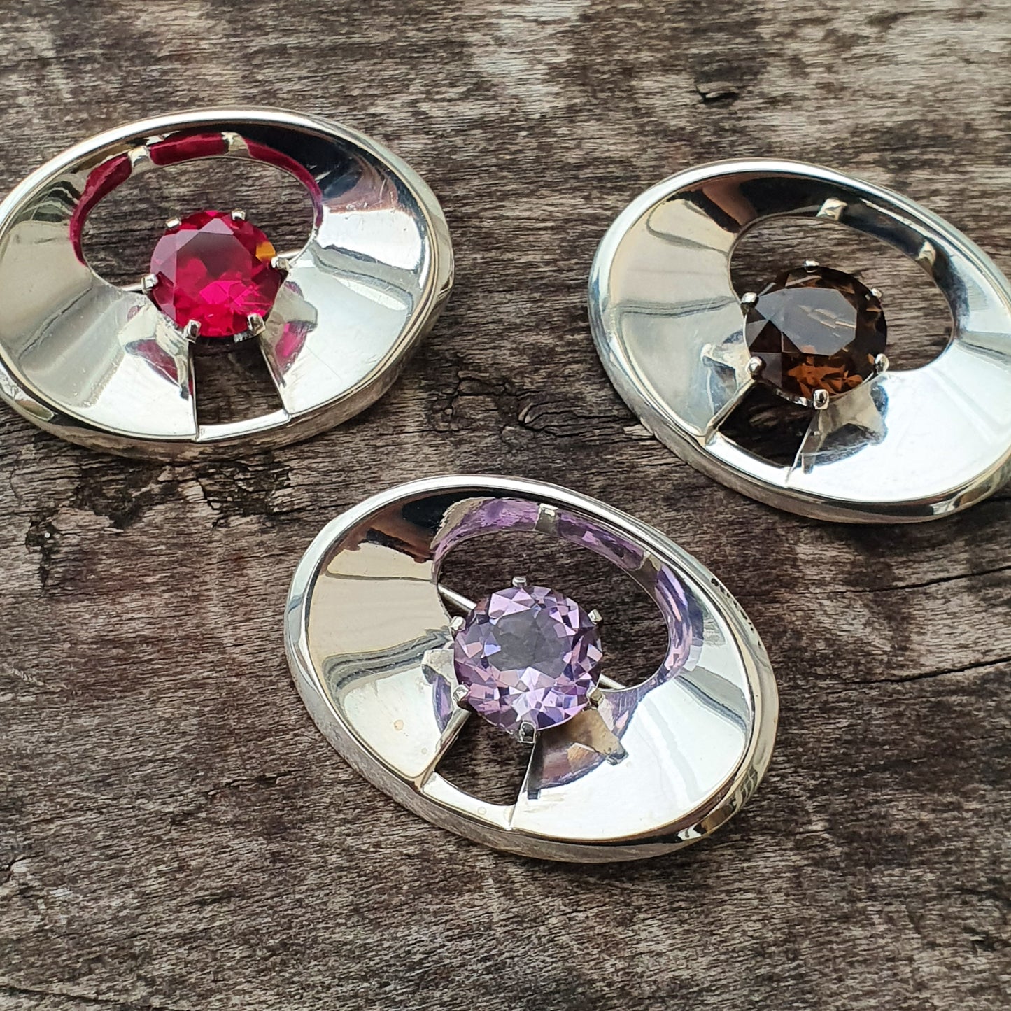 Three oval-shaped metal settings, each containing a different colored gemstone.