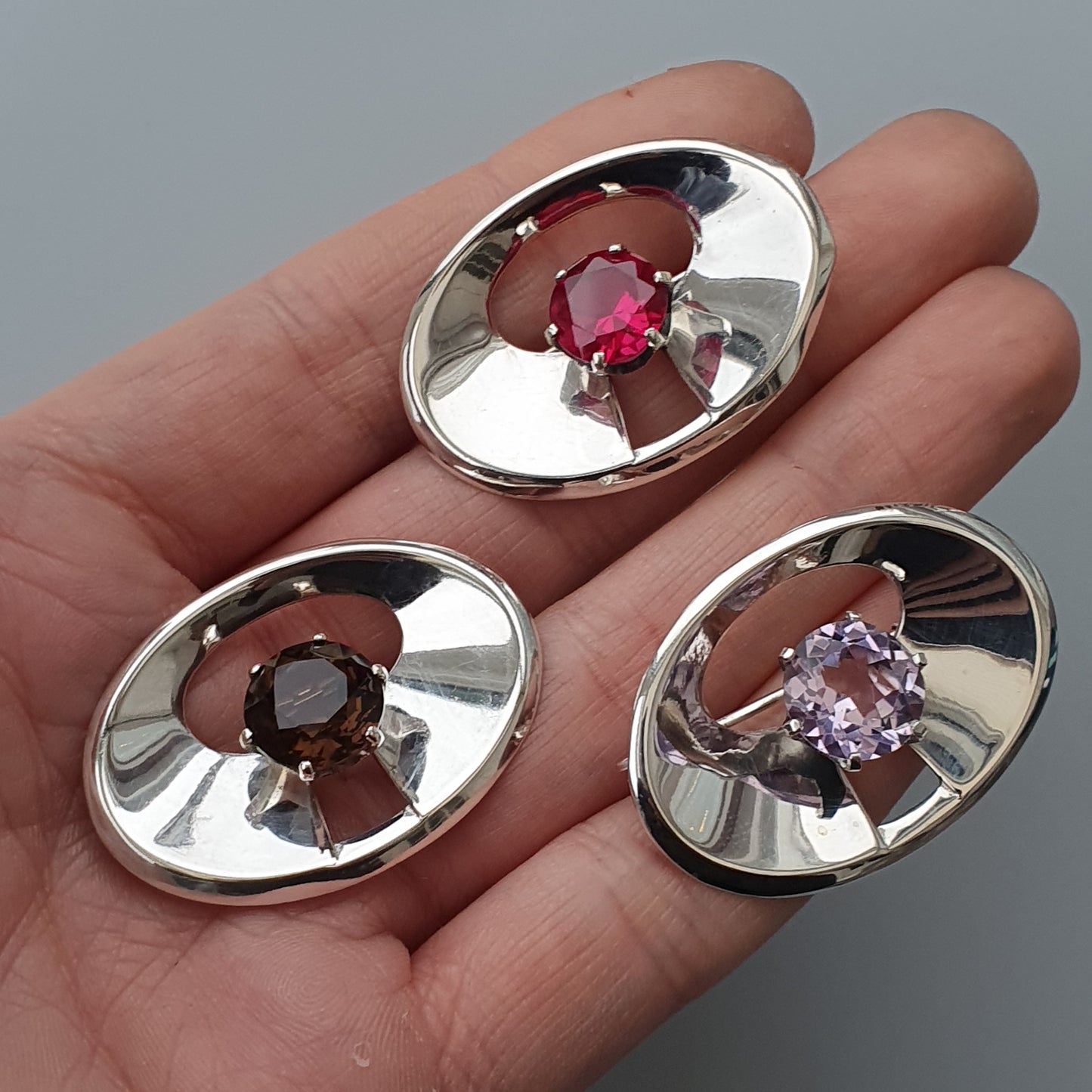 Three oval-shaped silver settings, each containing a different colored gemstone.