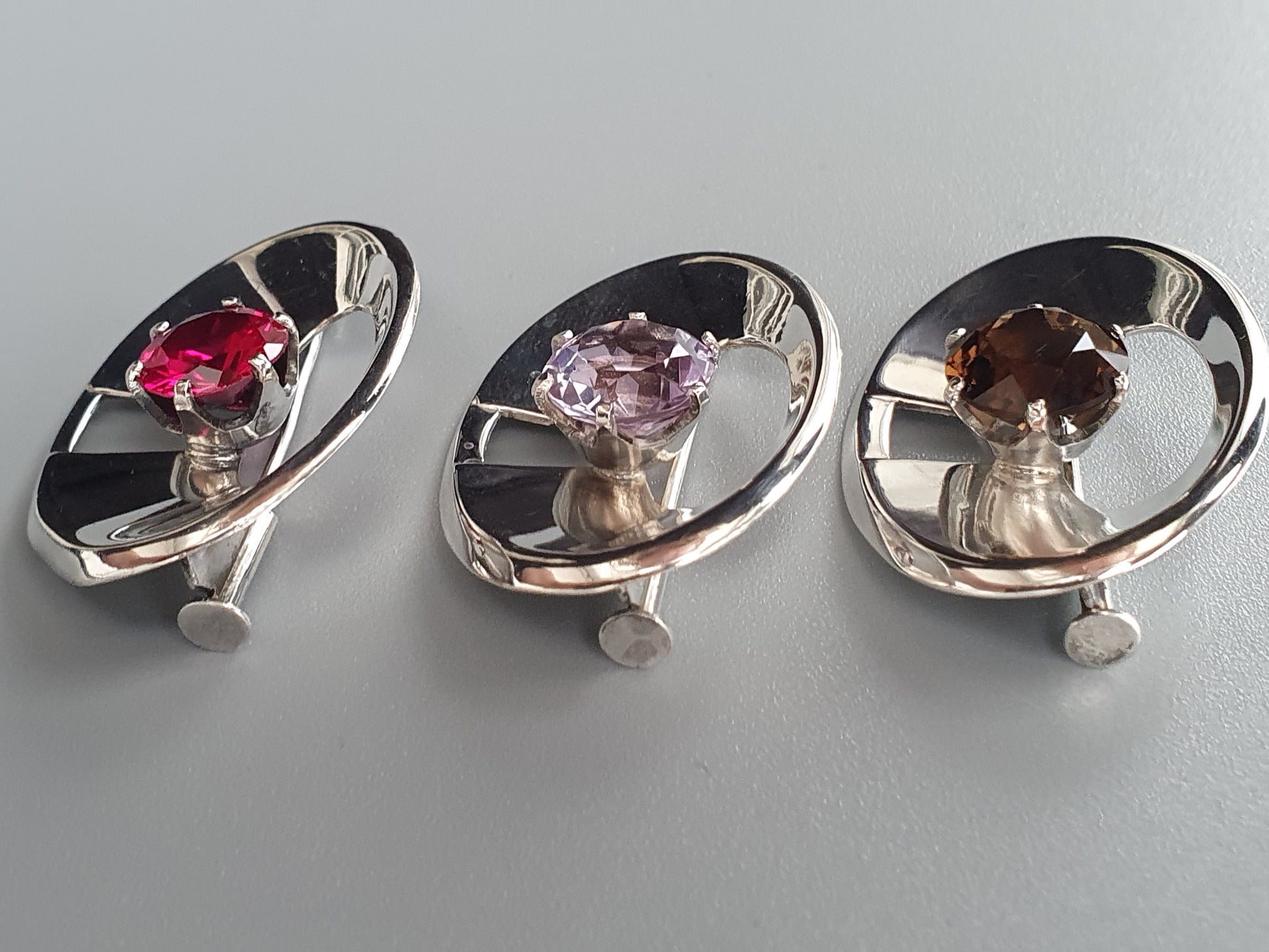 Three silver-colored jewelry pieces featuring gemstones set in oval-shaped designs.