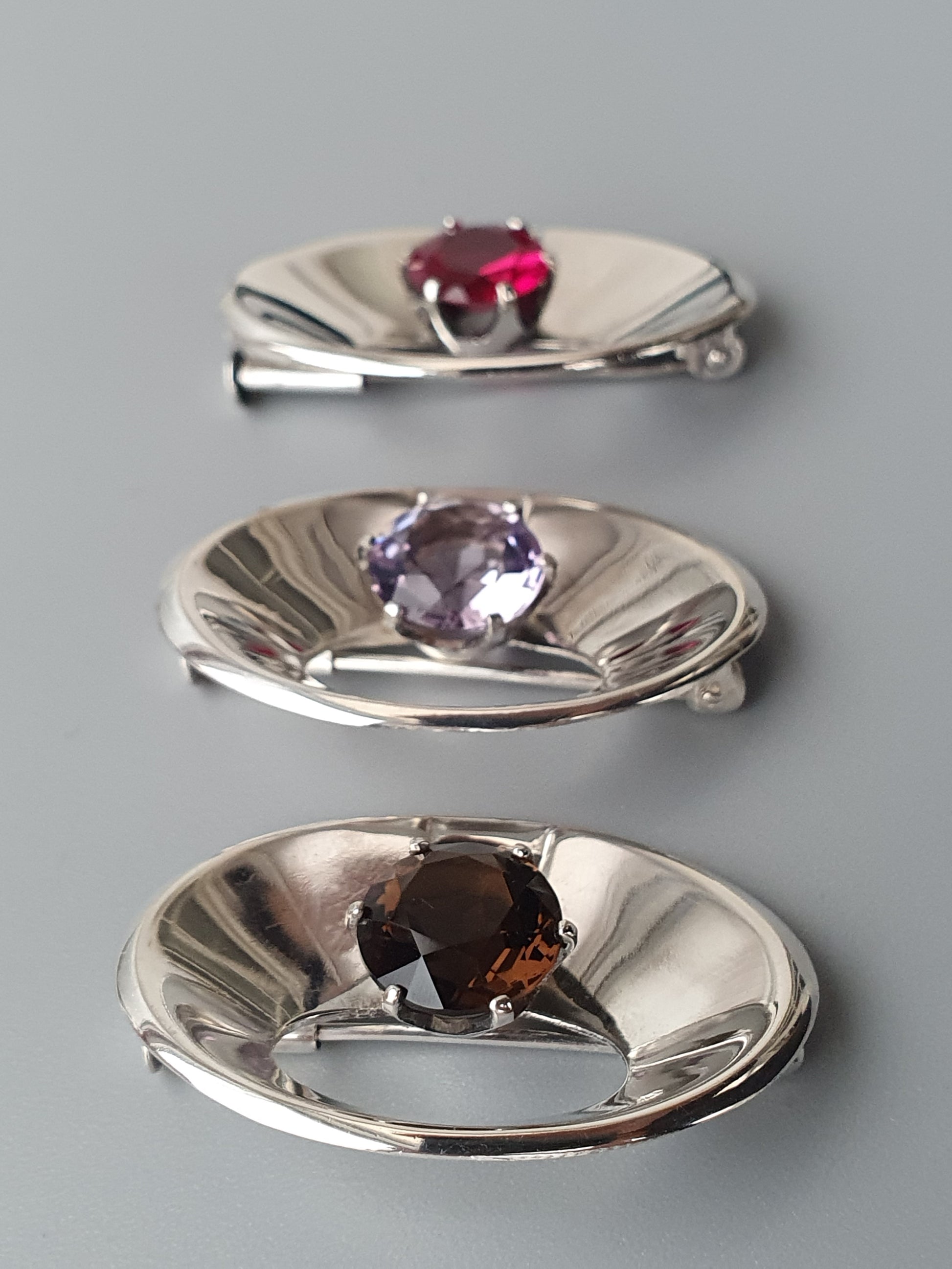 Three silver jewelry dishes or trays, each containing a different colored gemstone.