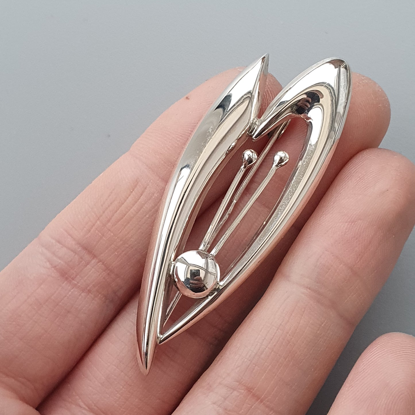 Sleek silver brooch with elongated leaf-like shapes and a central sphere.