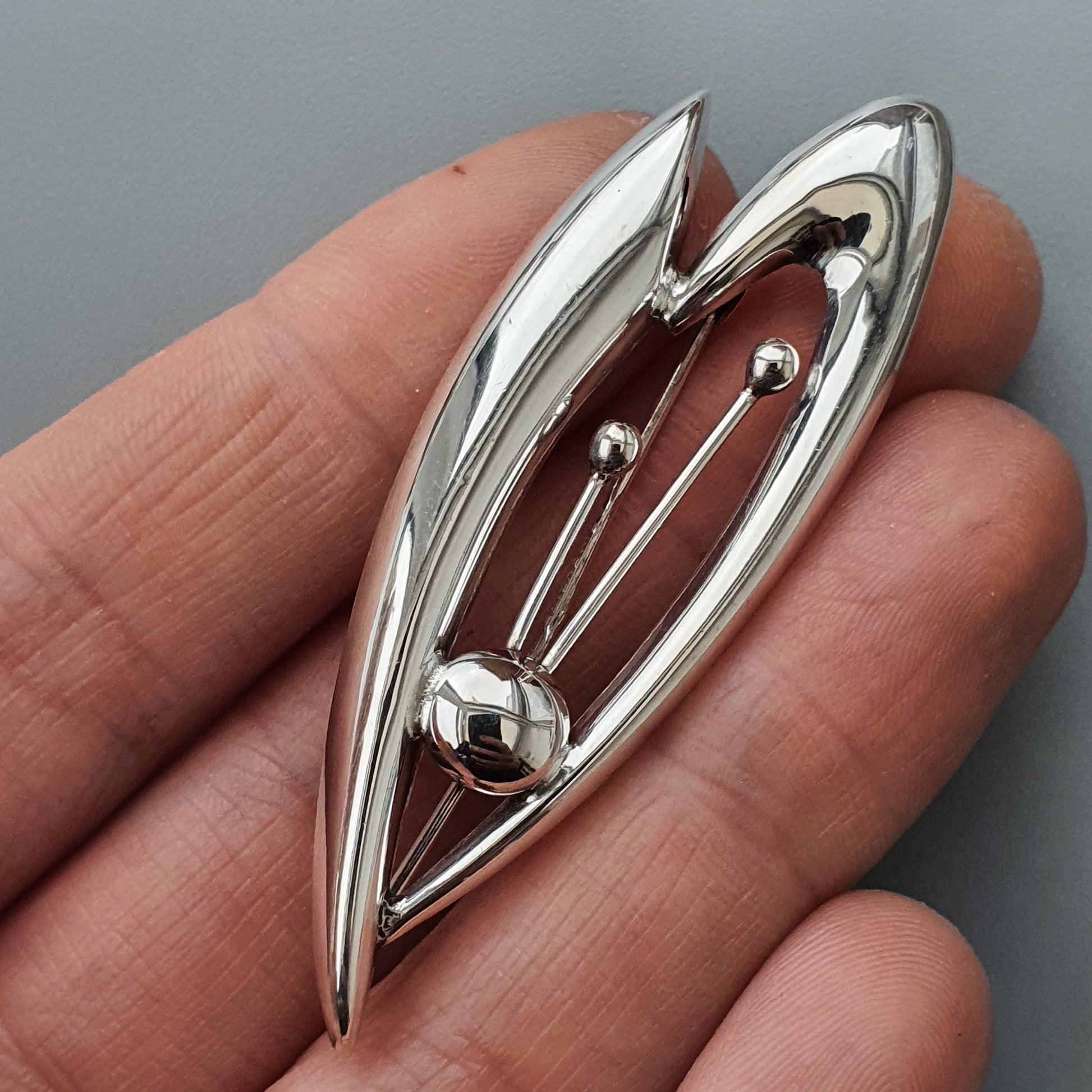 Silver leaf-shaped brooch or pin with a metallic ball accent.