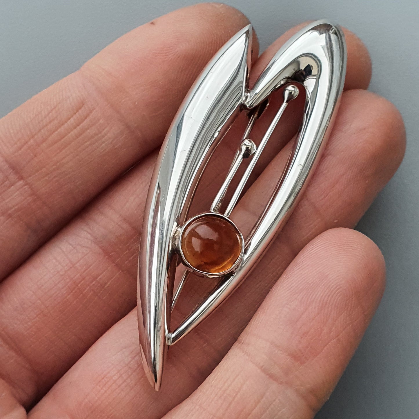 Silver brooch with an abstract leaf-like design featuring an amber-colored gemstone.