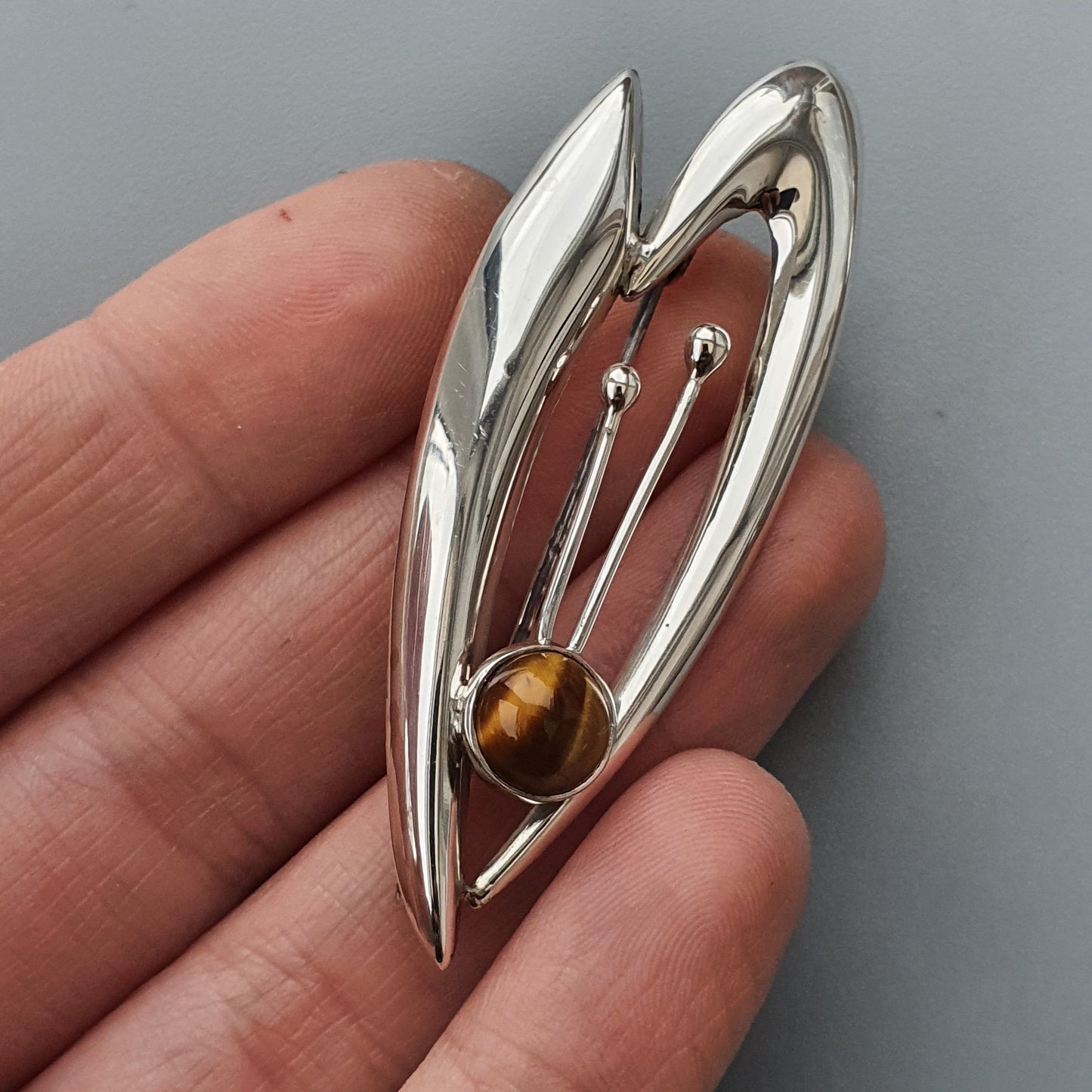 Silver abstract brooch or pendant with a tiger’s eye gemstone accent.