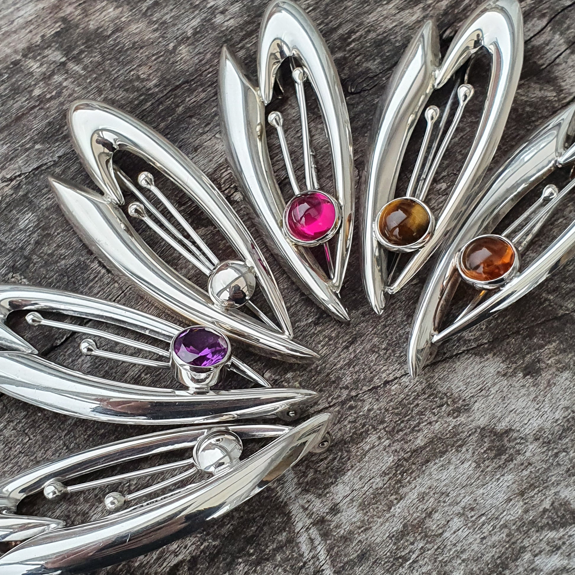 Silver leaf-shaped brooches or pendants with colorful gemstones set in their centers.