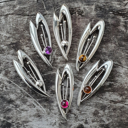 Silver leaf-shaped brooches or pendants with colorful gemstones set in their centers.