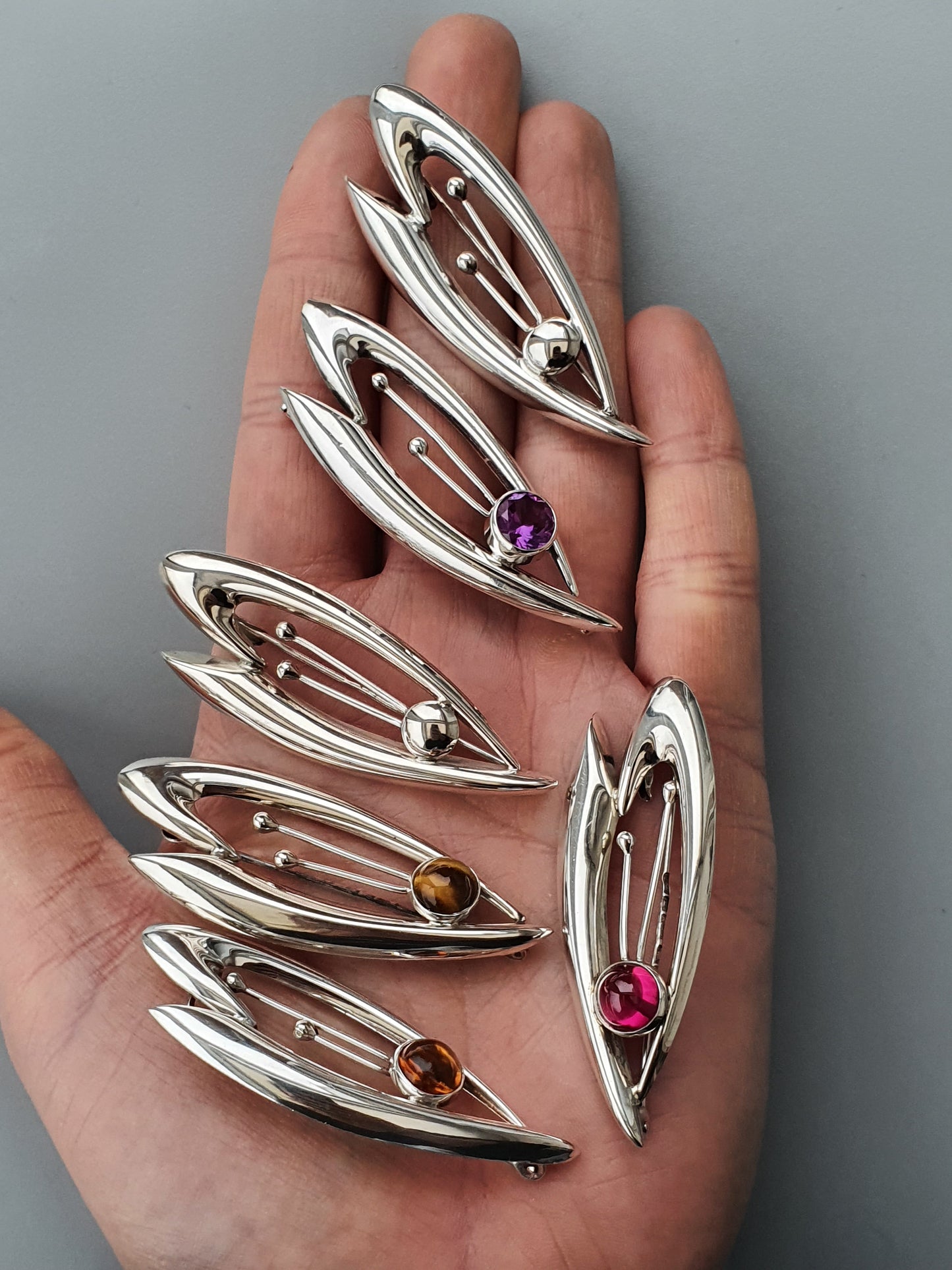 Silver leaf-shaped brooches or pins with colorful gemstones set inside each one.