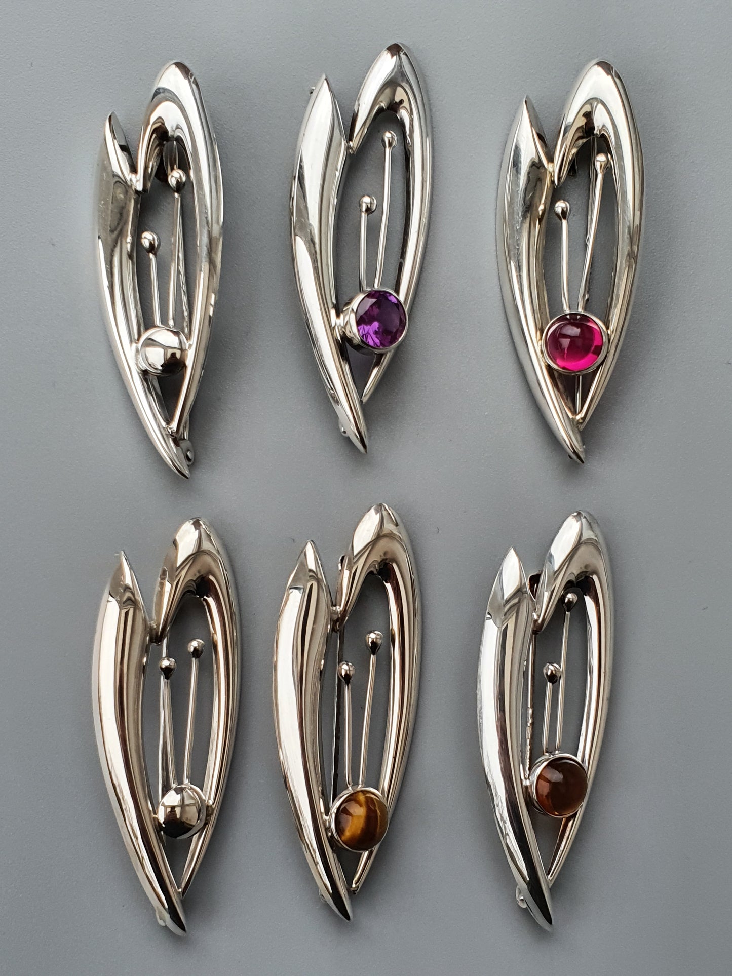 Set of six silver-toned teardrop-shaped pendants or brooches, each with a different colored gemstone.