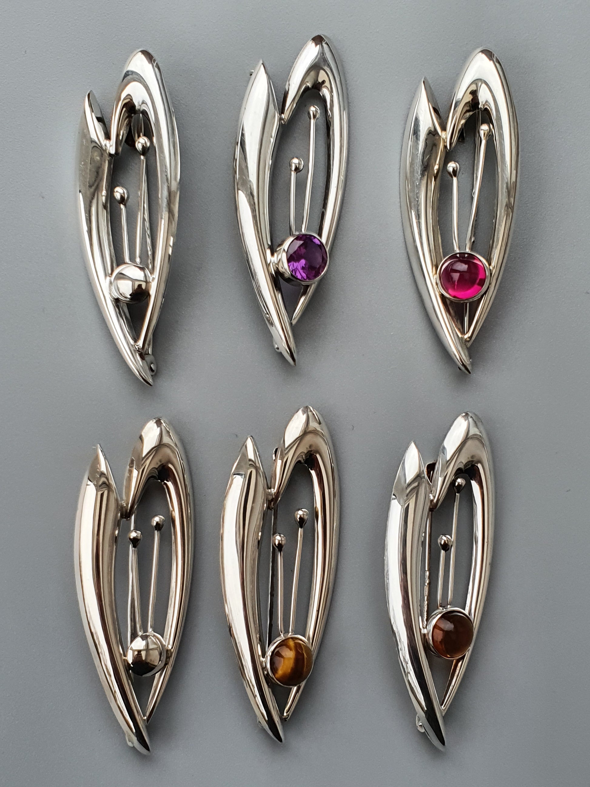 Set of six silver-toned teardrop-shaped pendants or brooches, each with a different colored gemstone.