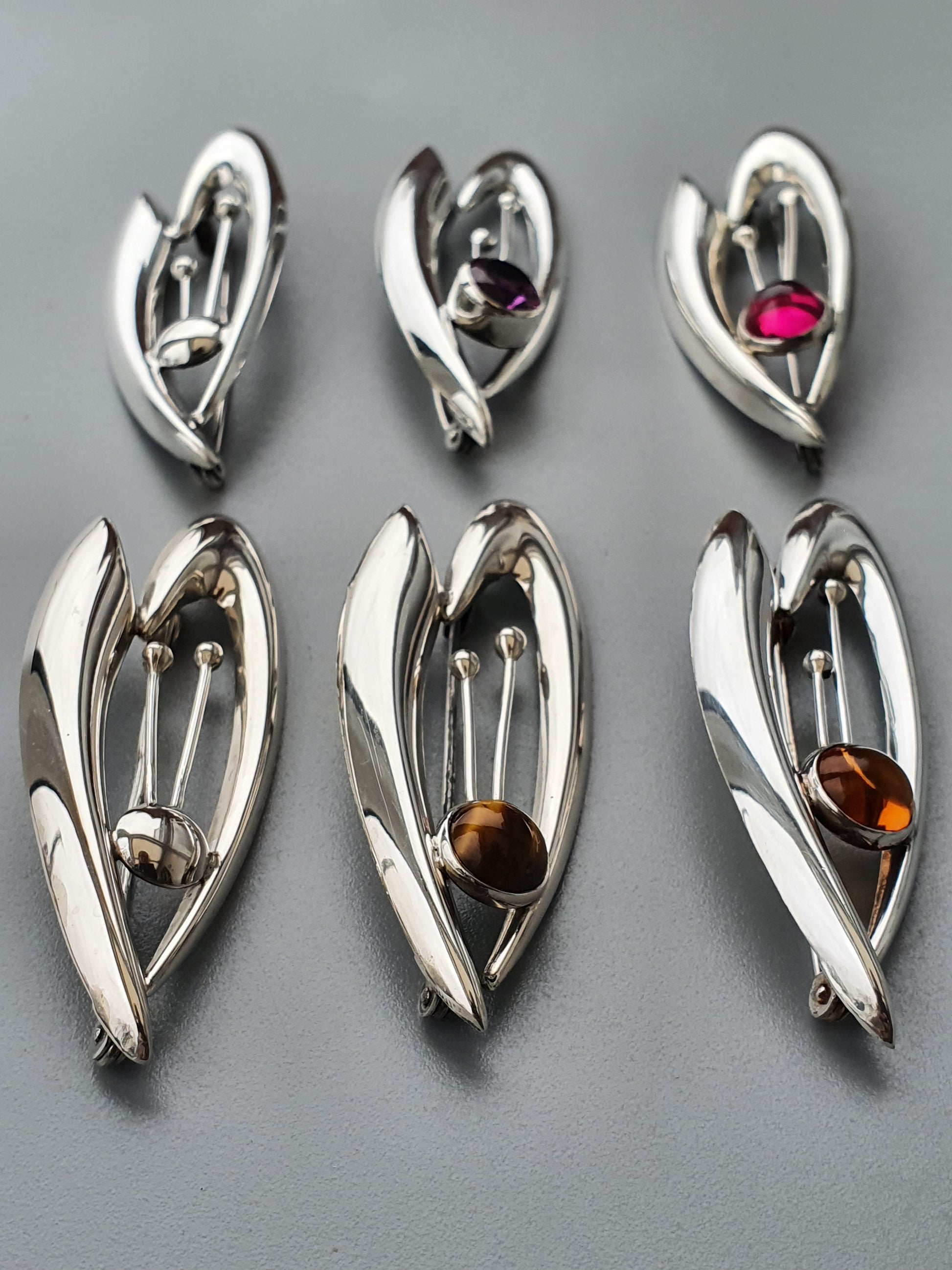 Silver pendants shaped like stylized leaves or petals, each containing a colored gemstone.