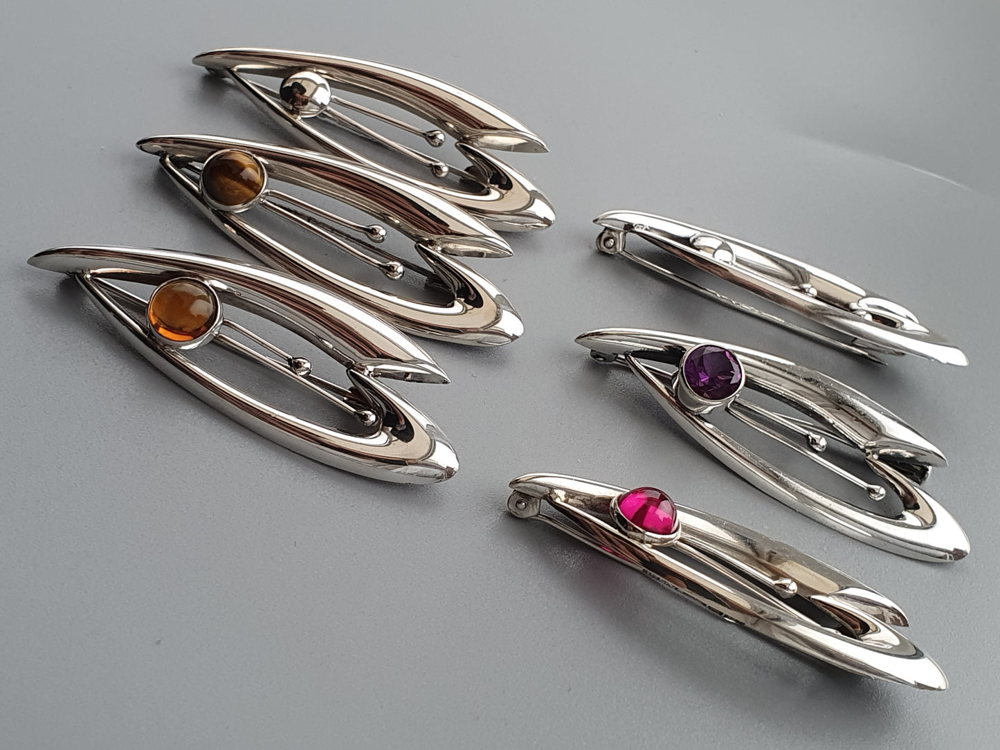 Collection of sleek, modern silver brooches with colorful gemstones.