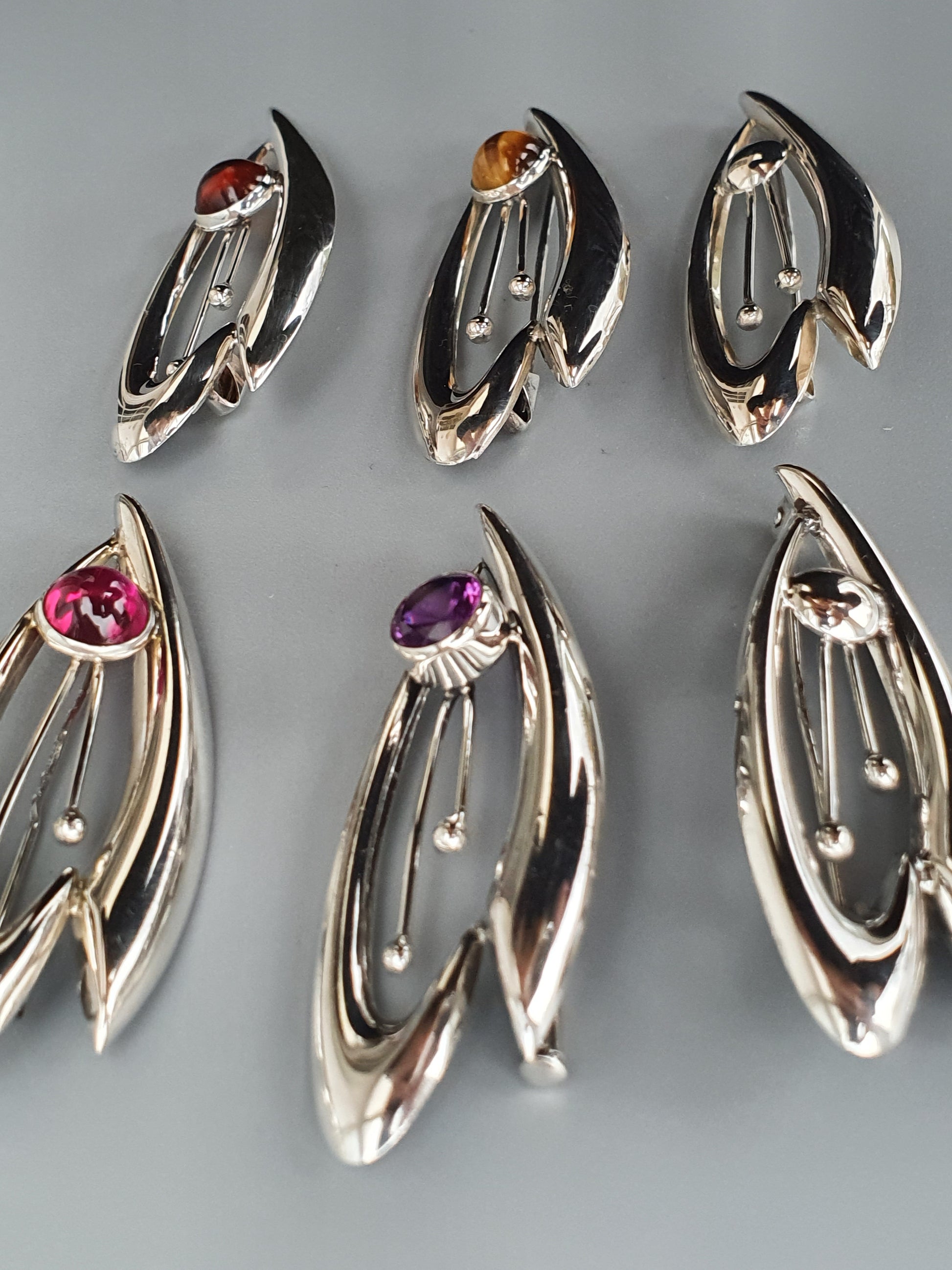 Set of six silver-toned jewelry pendants with gemstones in leaf-like designs.